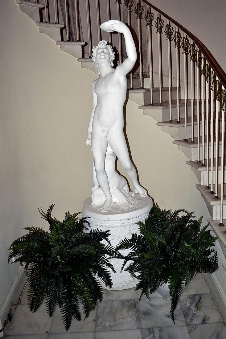 Parian Sculpture of a Man: Classical figure on a raised decorated pedestal depicting a nude male eating grapes with a cherub at his feet. 55" H, (23" at base).