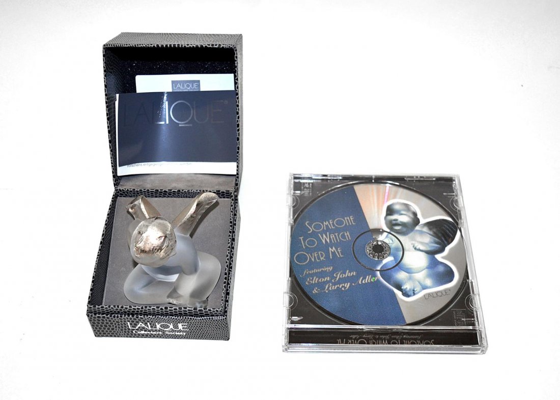 Lalique "Elton's Angel": Frosted crystal sculpture depicting a seared angel with gilt accents. 2.5"W x 2.75"D x 3"H. In very good condition. Accompanied by original presentation box and music CD. Signed on bottom.
