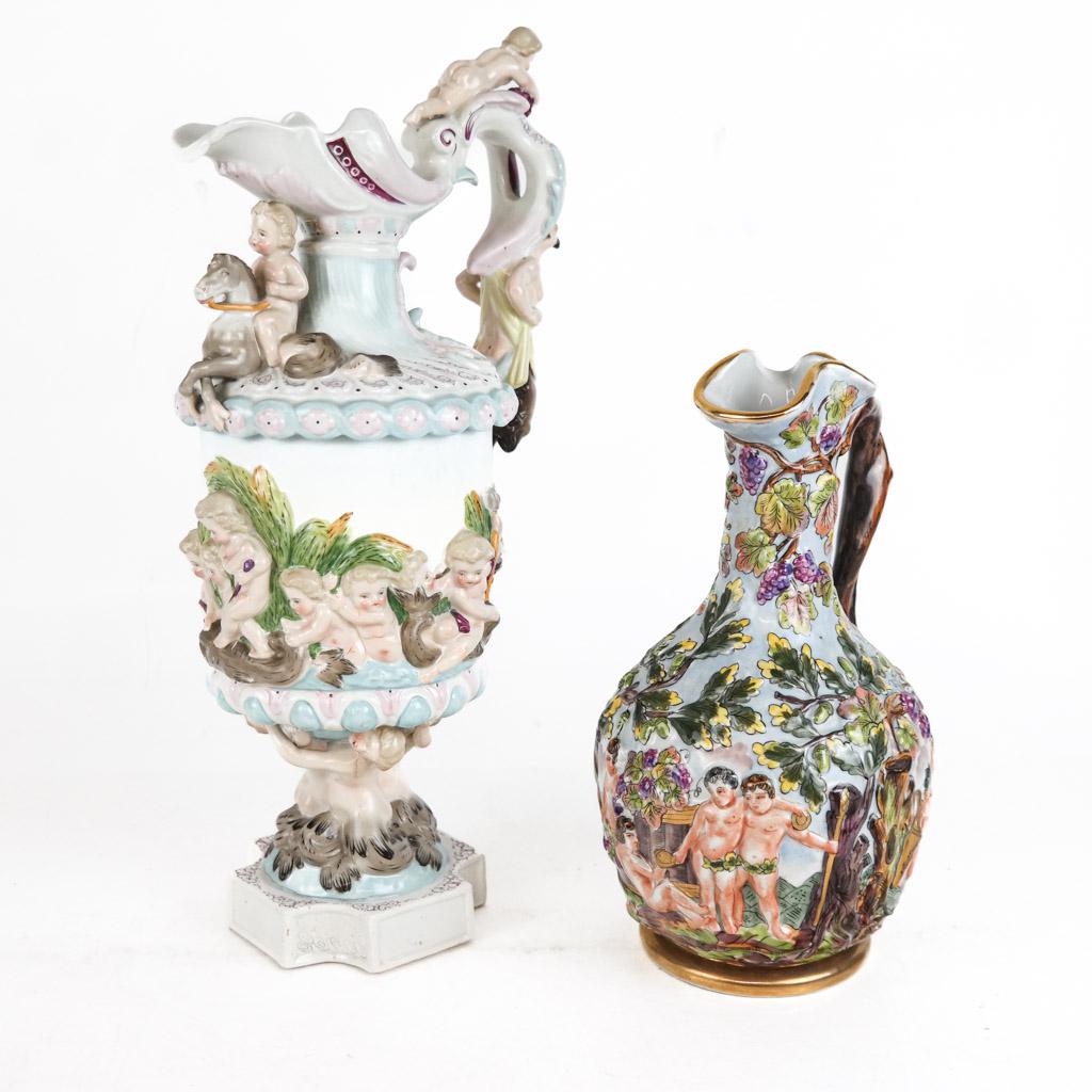 Two Capodimonte Wine Jugs: Two Capodimonte porcelain wine jugs, marked with the company's logo, one with mythical creatures and cherubs, the other showing the harvesting of grapes. Both with underglaze blue marks. [Taller: 15 1