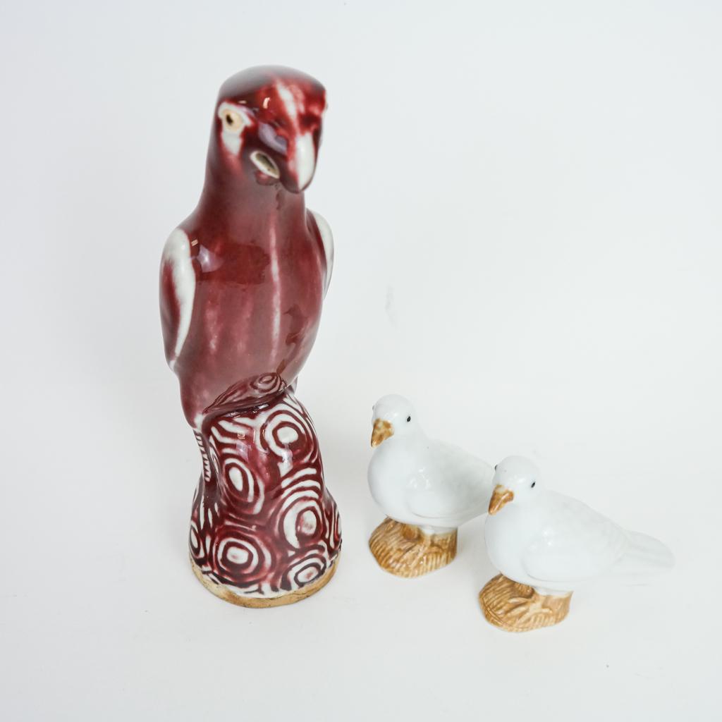 Chinese Oxblood Glazed Parrot & Two Birds: Chinese oxblood high glaze parrot with pierced beak and two smaller birds, probably doves, in white and brown. [Largest: 9 1/4" H x 3" W x 5" D]. All in good condition.