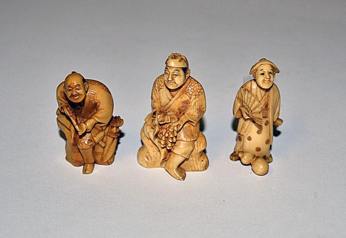 Three Ivory Netsukes: Two seated figures on plinths, together with a woman holding a fan. 2" H.