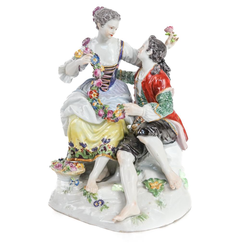 Meissen Porcelain Courting Couple Group: Group of a woman seated higher than the courting man, with flower garland and basket, marked and stamped on bottom. [7 1/2" H x 5 1/2" W x 4 1/2" D]. Chips to flowers, otherwise in overall good condit