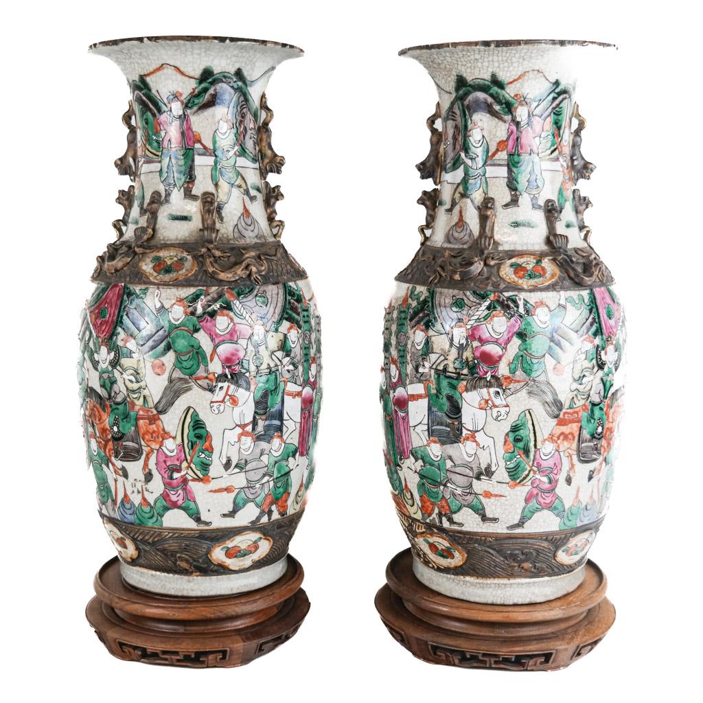 Chinese Pair of Canton Temple Vases: With relief decoration and scenic motifs of figures and horses in a procession, on pierced carved wood stands. [17 5/8 x 8 1/4 diam. inches]. Crackling and wear to glaze.