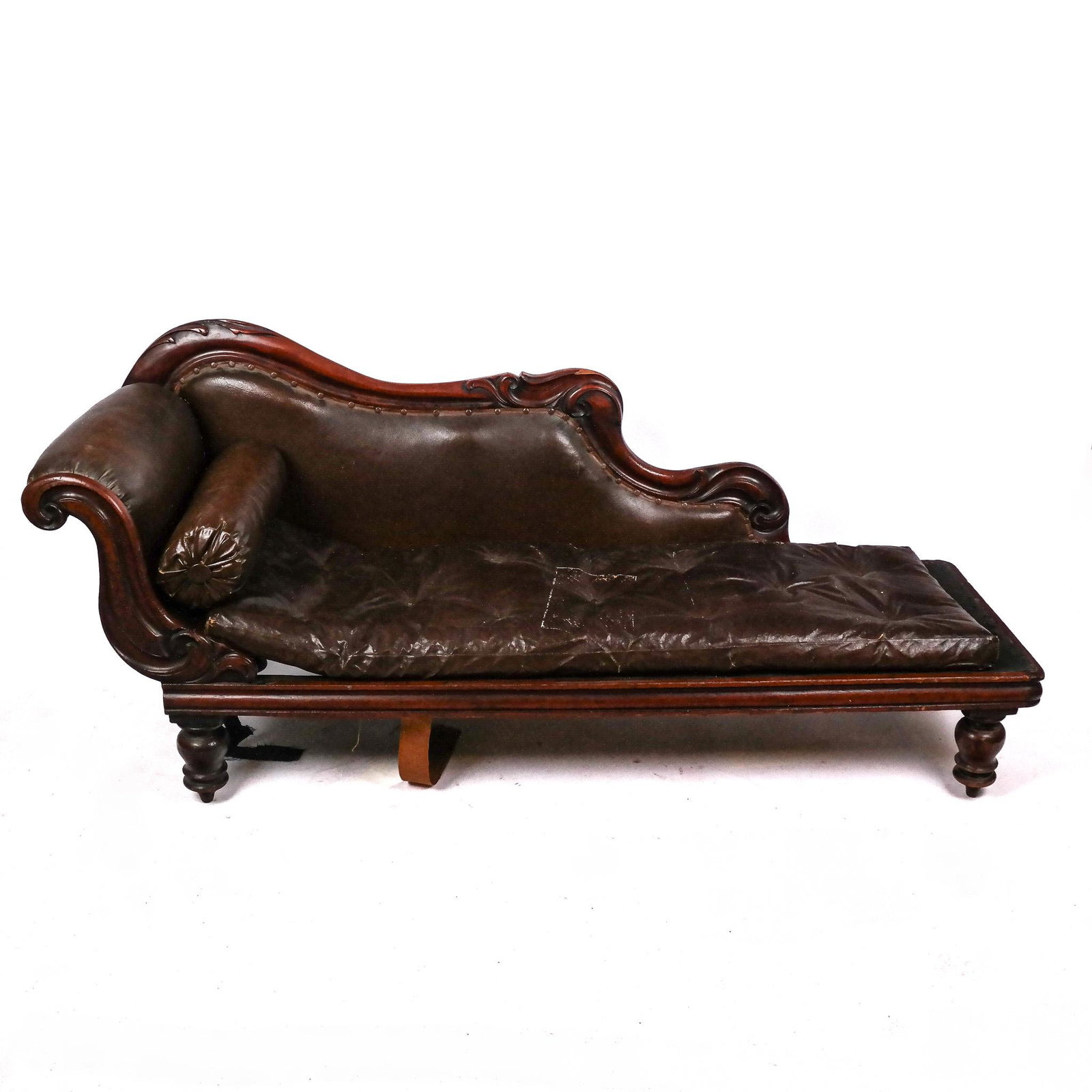 Victorian Carved Mahogany & Leather Recamier: Victorian carved mahogany and leather recamier, 19th century, the recamier / fainting couch with scroll-accented frame, raised on turned legs. [32" H x 75" W x 24" D]. In distressed condition with los