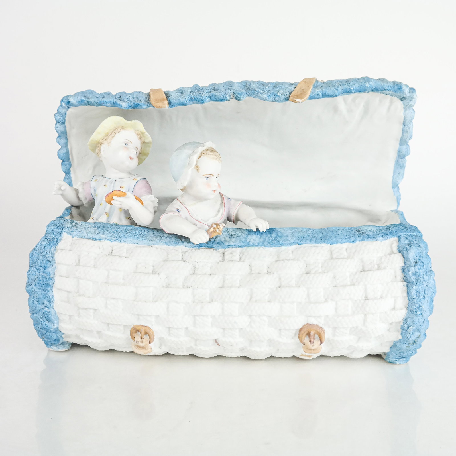 Whimsical Porcelain Figural Group: Whimsical porcelain figural group modeled as children in a basket. [8" H x 11 1/4" W x 4 1/2" D]. Residue, marks and wear.