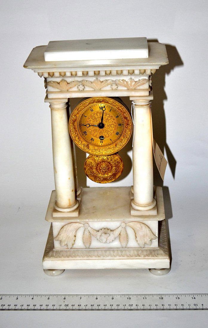 French Mantle Clock: White alabaster Empire-style mantle clock, Corinthian columns, bronze doré face and pendulum [top removable]. 15" H x 8 1/4" L. Chips.