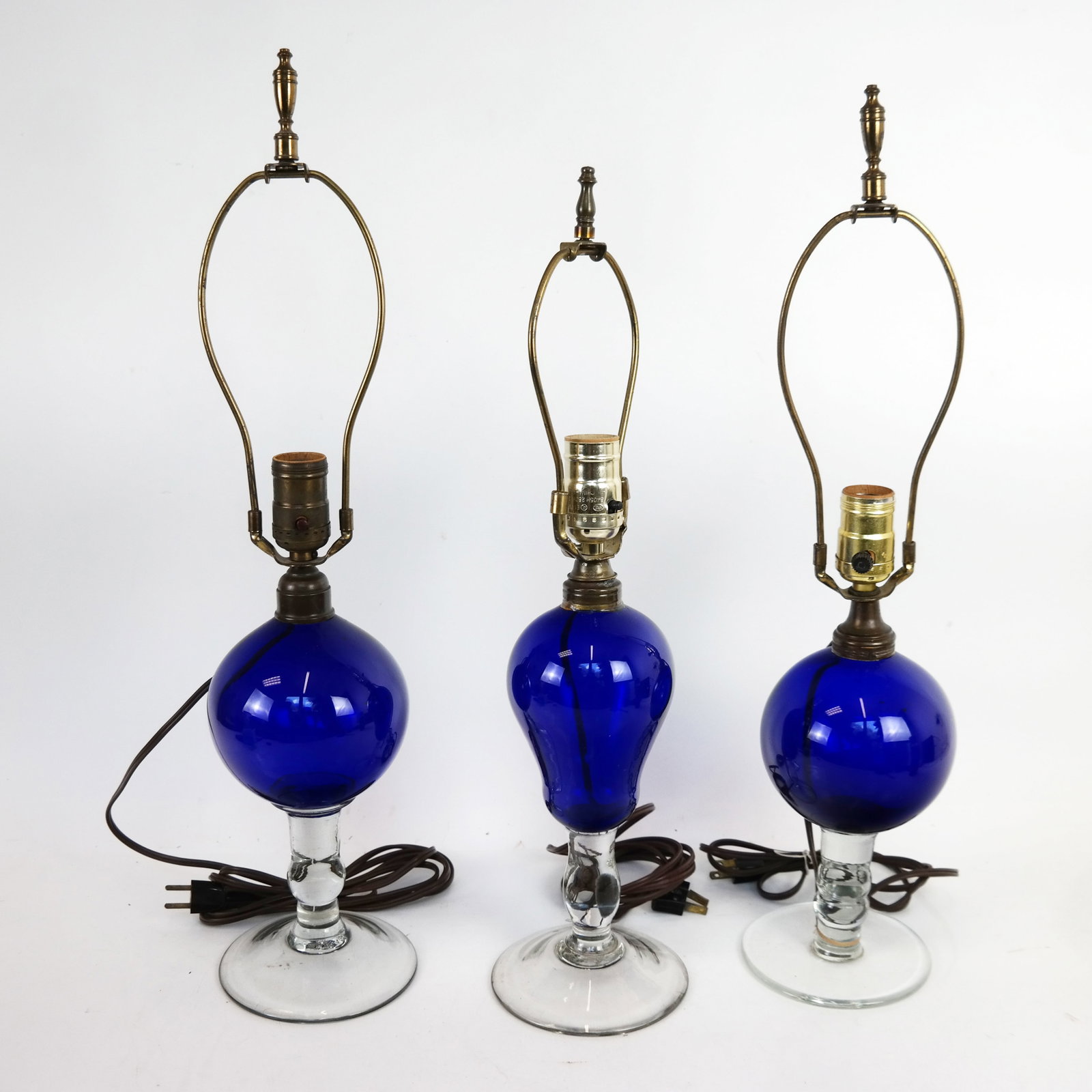 Three (3) Blue and Clear Glass Lamps: Three blue and clear glass bases with mounted lamp tops. [Tallest: 26" H to top of finial].