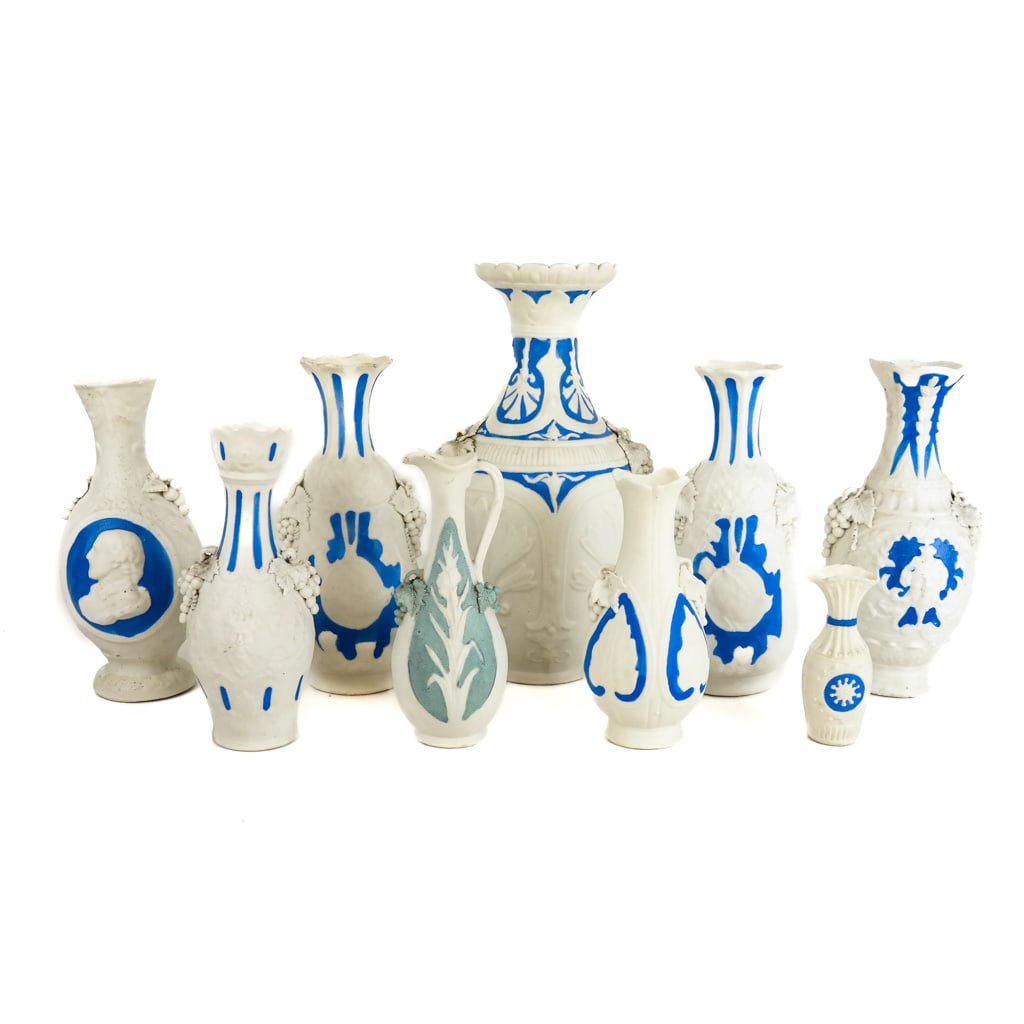 Group of 9 Parian Porcelain Relief Vases: Group of 9 parian porcelain relief vases, each with Bacchanalian motifs of grapes and leaves, in the manner of Bennington; unmarked, with applied blue paint decoration. [Tallest: 10 7/8" H x 6 1/4" Di