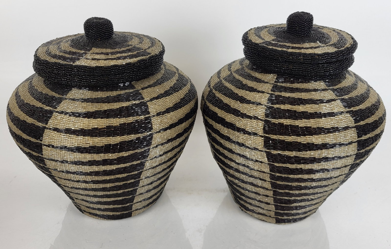 Pair of Beaded Storage Jars by Bindah: Pair of beaded storage jars by Bindah for Neiman Marcus, designed as Indonesian covered baskets, with original retail tags. [11 1/4" H x 10 1/4" Diam.]. Minor wear.