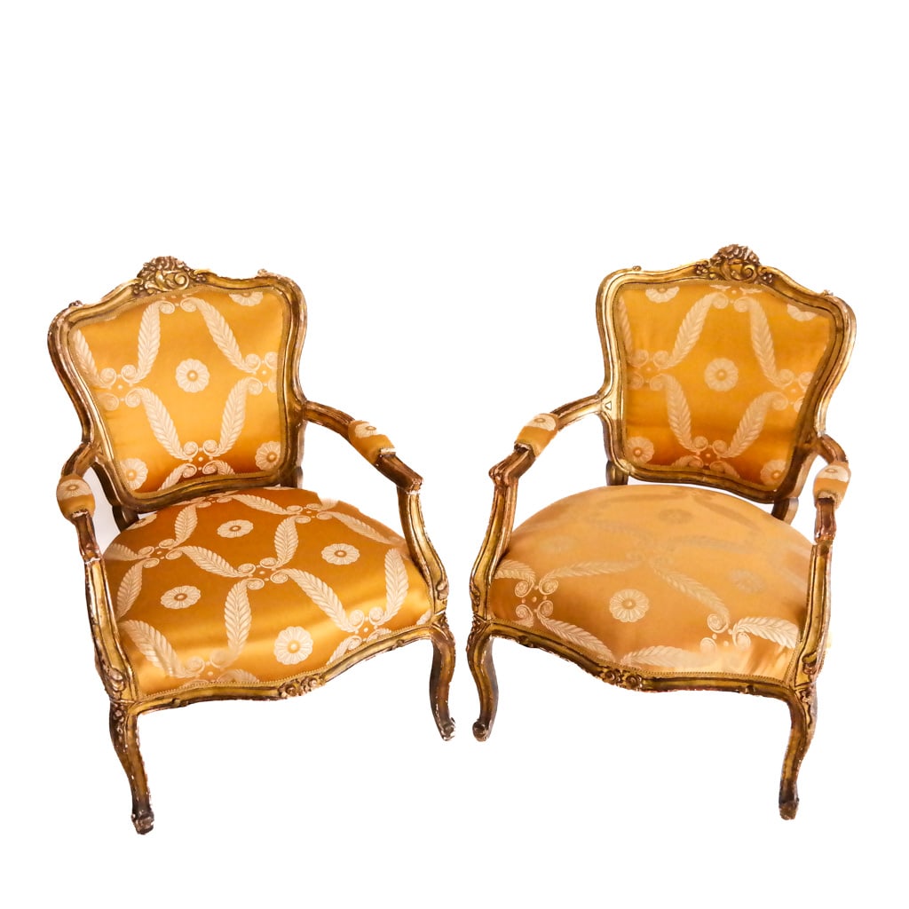 Pair French Carved Gilt Armchairs: Pair of Louis XV-style giltwood open armchairs with floral carved crests and gold leaf design upholstery. [37 H x 27 W x 26 D inches, 16 inches to seat].