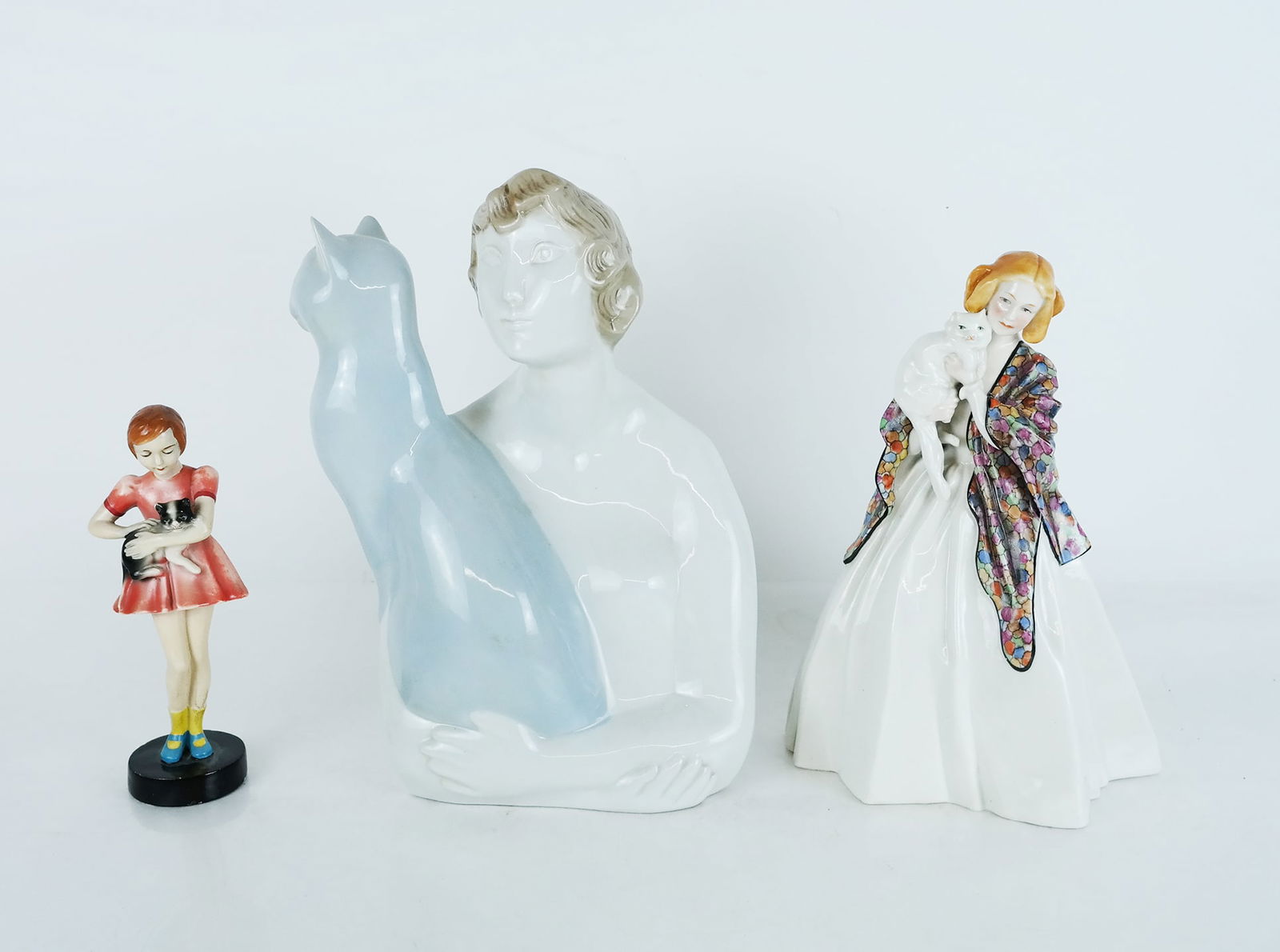 Three Figural Painted Porcelain Sculptures: Three (3) figural painted porcelain sculptures, modeled as ladies alone holding their cat, by Royal Dux, Coimbra and another, marked to bases. [11 1/4" H x 9" W x 5" D].