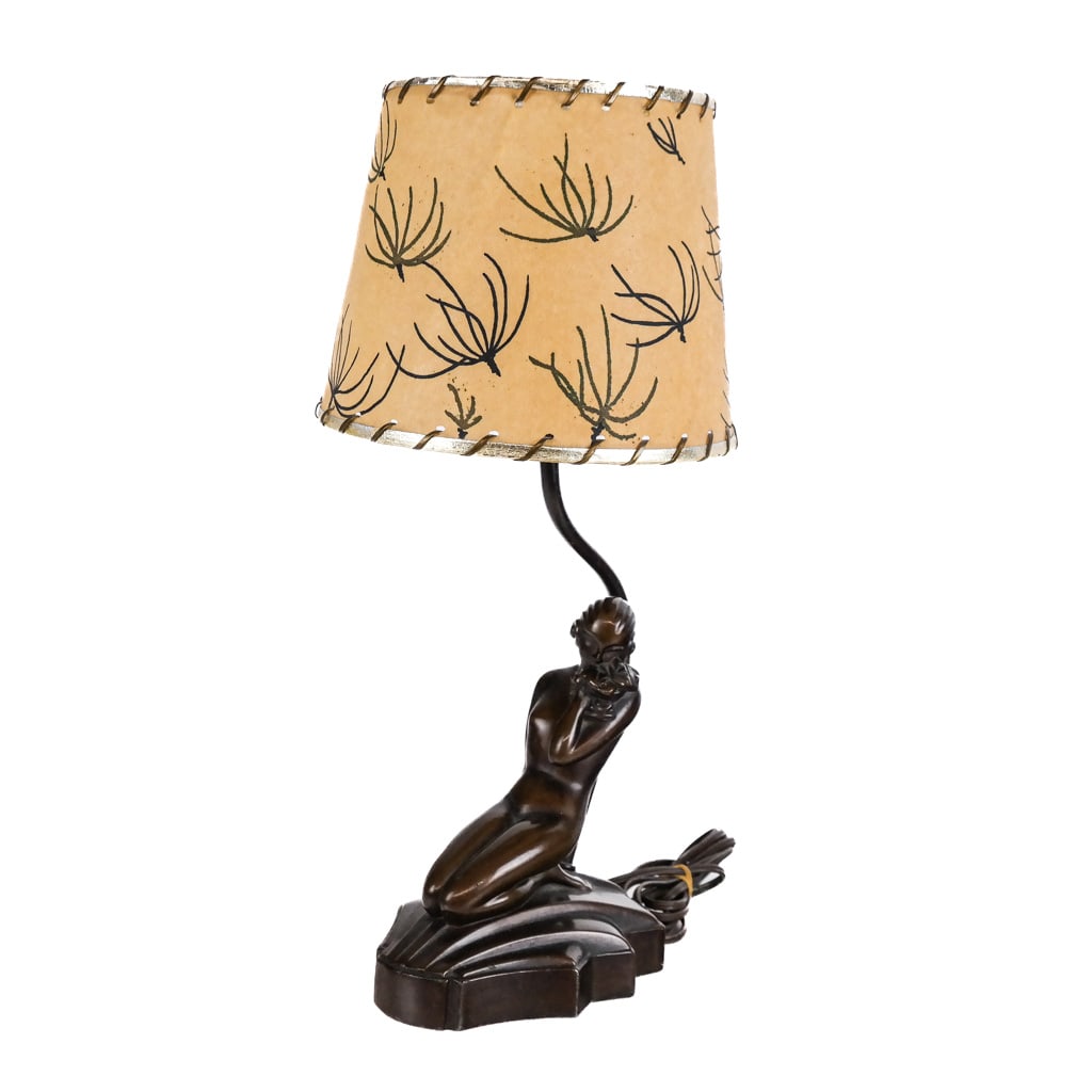 Art Deco Nude Bronze Lamp: Art Deco bronze lamp, circa 1930s, modeled as a kneeling nude, with associated clip-on paper lampshade. [Lamp to socket: 13 1/2" H x 6 3/4" W x 4 3/4" D]. Losses to finish and patina.