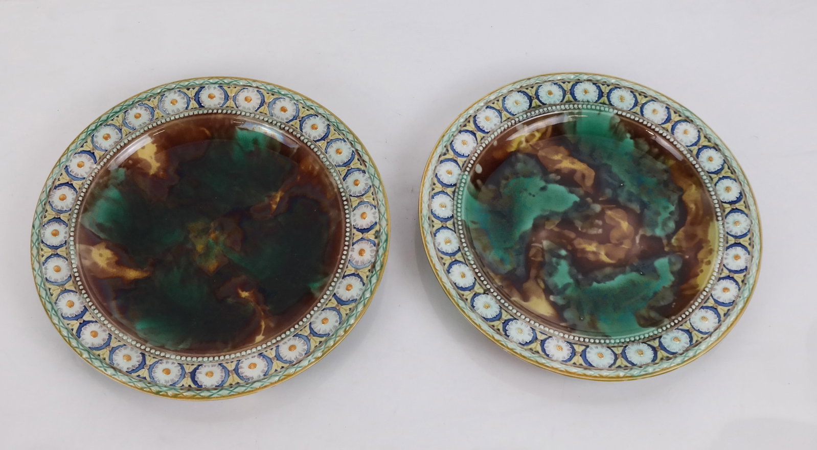 Wedgwood English Majolica Plates (2): Two Wedgwood English majolica plates, late 19th century, each with daisy flower border around mottled swirled glaze, the base marked "Wedgwood" and "VMA" or "QSZ", respectively. [8 7/8" Diam.]. Both w