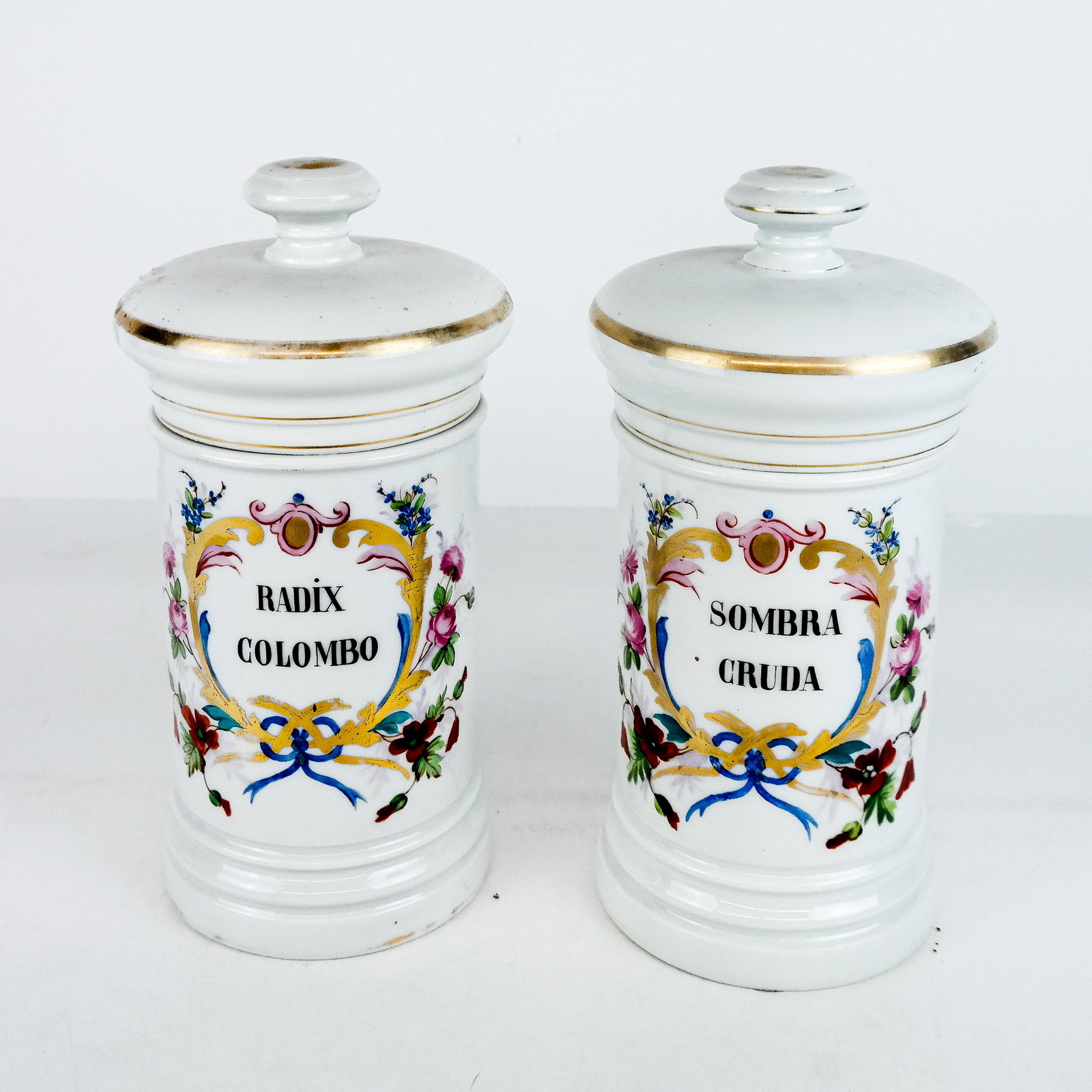 Pair of Floral Opaline Apothecary Jars: Pair of floral decorated jars with lids: "Radix Columbo" and "Sombra Cruda". [10" H (including cover); 6 3/4" H (without cover)]. Both with wear.