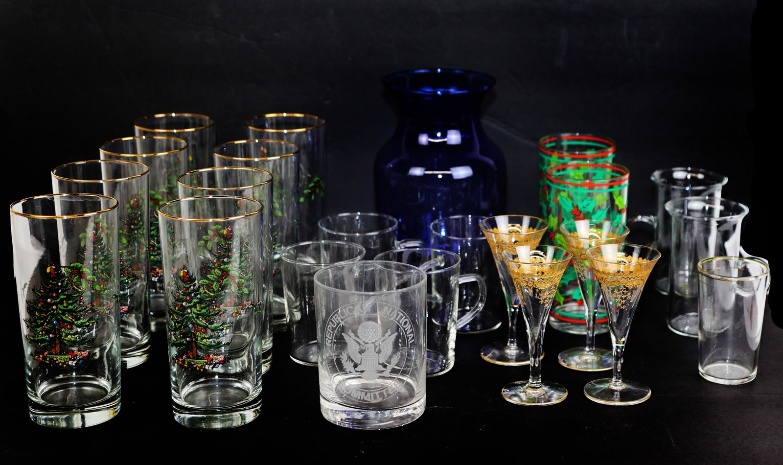 Assembled Group of Glassware: Assembled group of glassware, including holiday tumblers, gilt-accented cordial liqueur glasses, a blue vase, and other items. [Vase: 8" H x 5" Diam.].