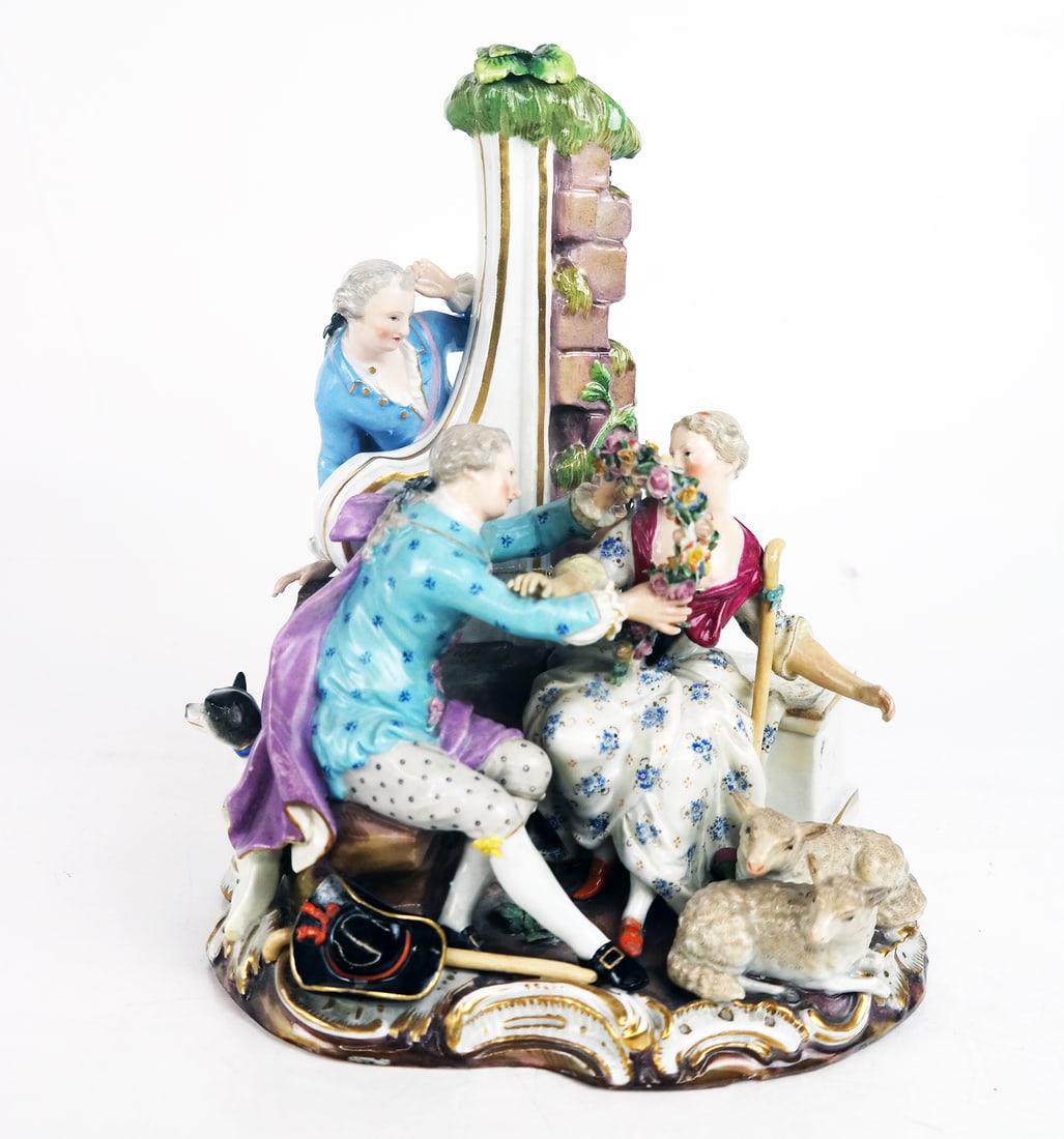 Meissen Figural Courting / Pastoral Group: Meissen porcelain group comprising a man and woman with wreath and lambs, and an onlooker with a dog, all by a rock and scroll post. [9 1/2" H X 8" W X 8" D]. Restorations.