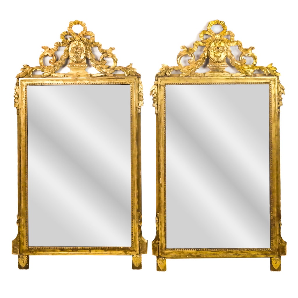 Pair of Louis XVI-Style Giltwood Mirrors: Pair of Louis XVI-style giltwood mirrors, 19th century, each with foliate and ribbon crest. [51" H x 28" W]. Later refreshing to gilding, scattered hairline cracks and losses to carving, backs with ag