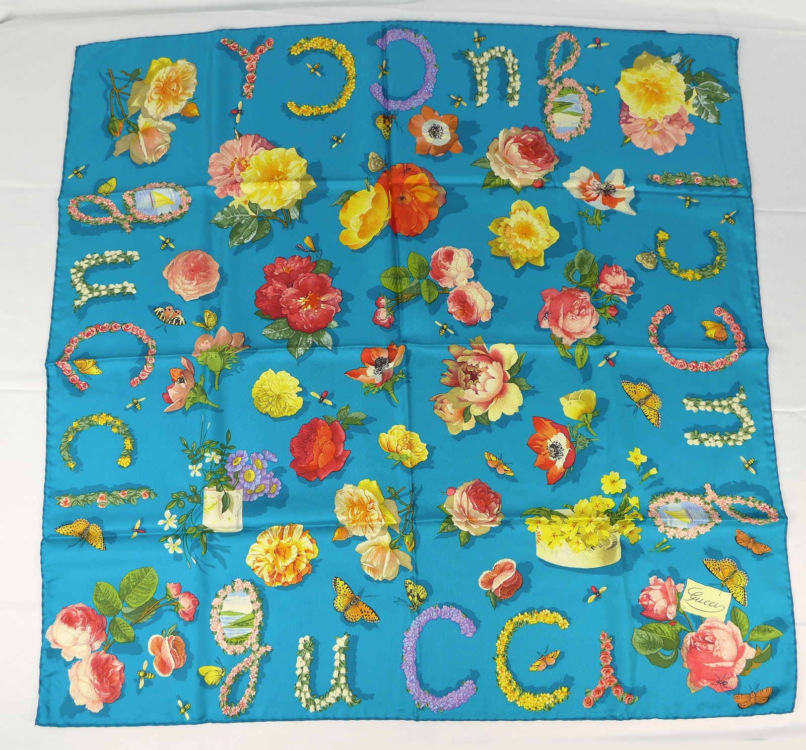 Vintage Gucci Italy Silk scarf New with tags and box "Flowers and Insects": This is a Gucci Silk Scarf made in Italy dating from the 1990's early 2000's. Decorated with multiple flowers and insects bordered with the Word gucci spelled out in flower design. In new condition wi
