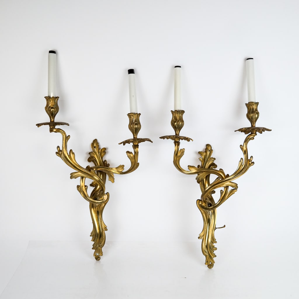 Pair of Louis XV-Style Gilt Bronze Sconces: Pair of Louis XV-style gilt bronze sconces, 20th century, the two-light bras de lumieres with upswept arms and rocaille scrolling details. [24 1/2" H x 13" W x 5" D].