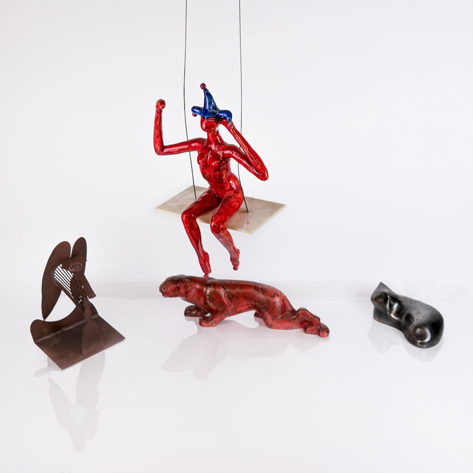 Four Assorted Sculptures: Four (4) assorted sculptures, comprising a marbleized composition jaguar, a metal maquette after Picasso, a ceramic cat, and a plastic, ceramic and metal jester on a swing.