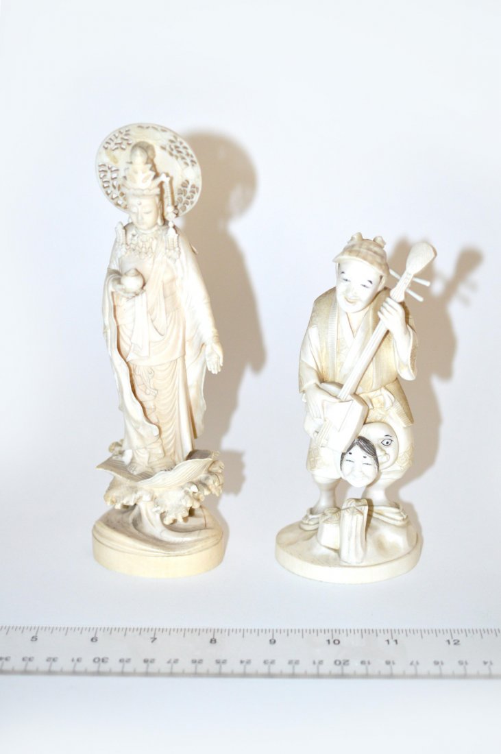 Two Asian Carved Ivory Figures: Comprises a female deity with pierced halo standing on a lotus leaf atop a cresting wave. 2 1/2" W x 2" D x 8 3/8" H. Loss to headdress. With a smiling musician bearing two masks. 2 3/4" W x 2 1/4" D 