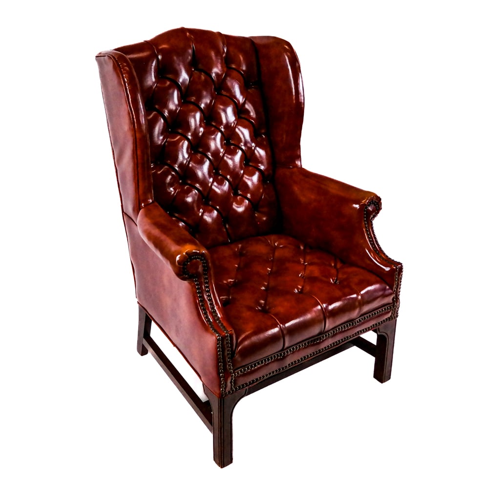 Georgian-Style Tufted Library Armchair: Georgian-style tufted library armchair, having a winged back over rolled arms, overall with Chesterfield button tufting and nail head trim, raised on carved mahogany legs. [42" H x 30 1/2" W x 26" D].