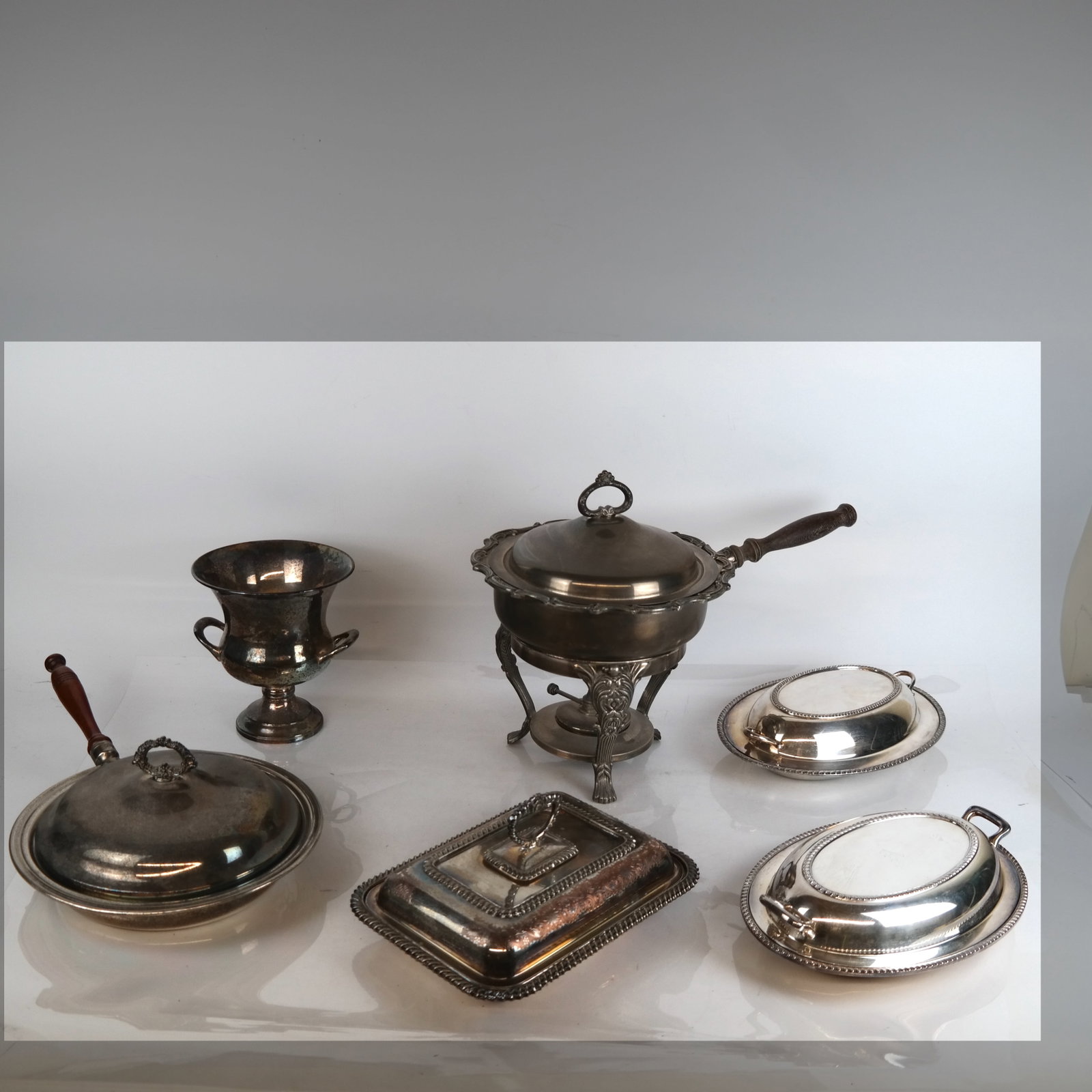6 Silver Plate Articles: Six (6) silver plate articles, including three covered vegetable dishes, a warming dish on stand, a wine bucket, and a chafing dish with wood handle.