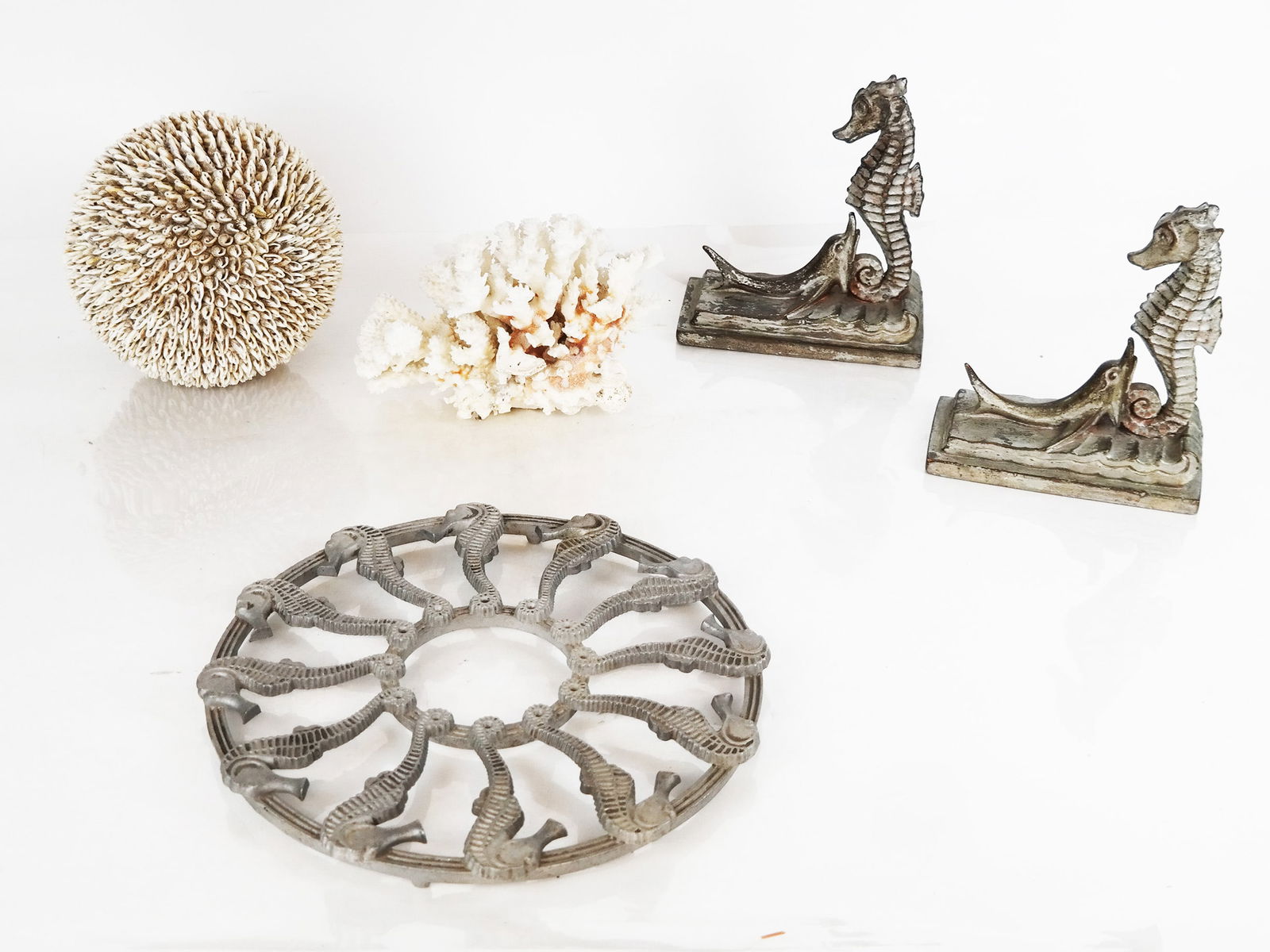 Group of Nautical Motif Accessories (5): Group of nautical motif accessories, comprising a pair of composition seahorse and dolphin bookends, a seahorse metal trivet, a branch coral cluster, and cowrie shell sphere bookends. [7 3/8" H x 6 1/