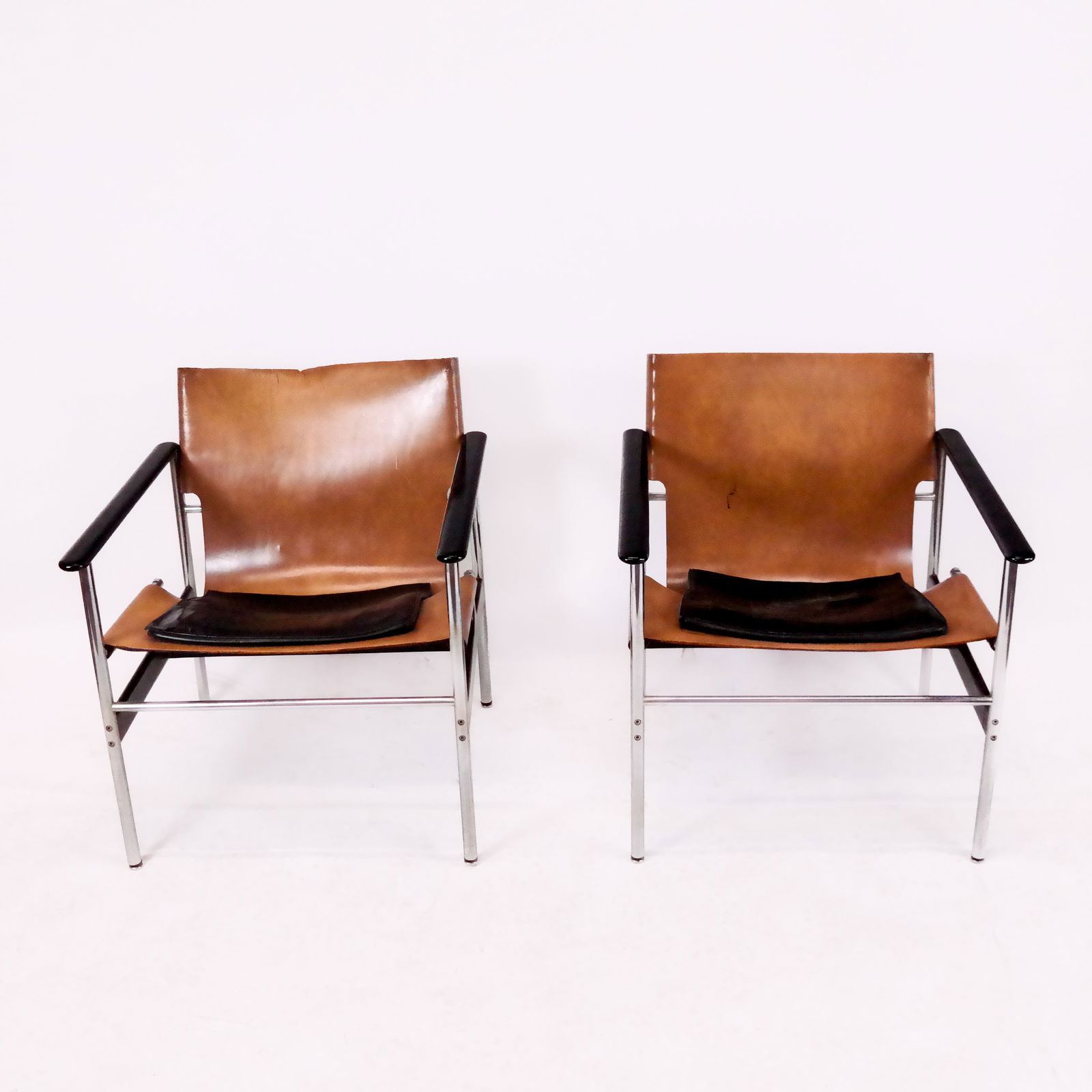 Pair of Knoll Pollock Leather Open Armchairs: Pair of Knoll vintage "sling" lounge chairs, designed by Charles Pollock, bearing labels to base. [28 3/8" H x 23" W x 25" D]. Leather worn, dried and cracked at edges; metal with oxidation and dents.