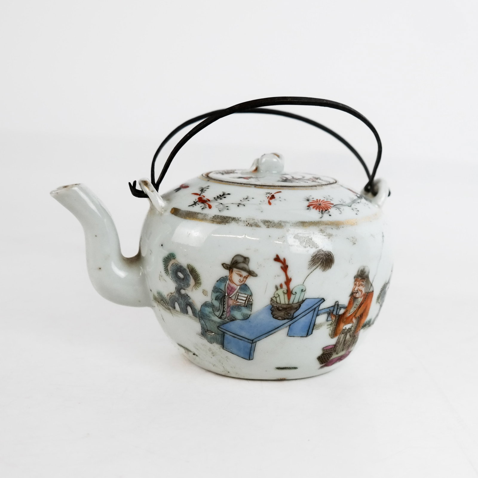 Chinese Porcelain Teapot: Antique Chinese porcelain teapot depicting figures in a landscape, with metal handle. [5" H x 5 1/4" W x 4 1/8" D (including handle)]. Wear evident commensurate with age; chips to lid; wear and losses