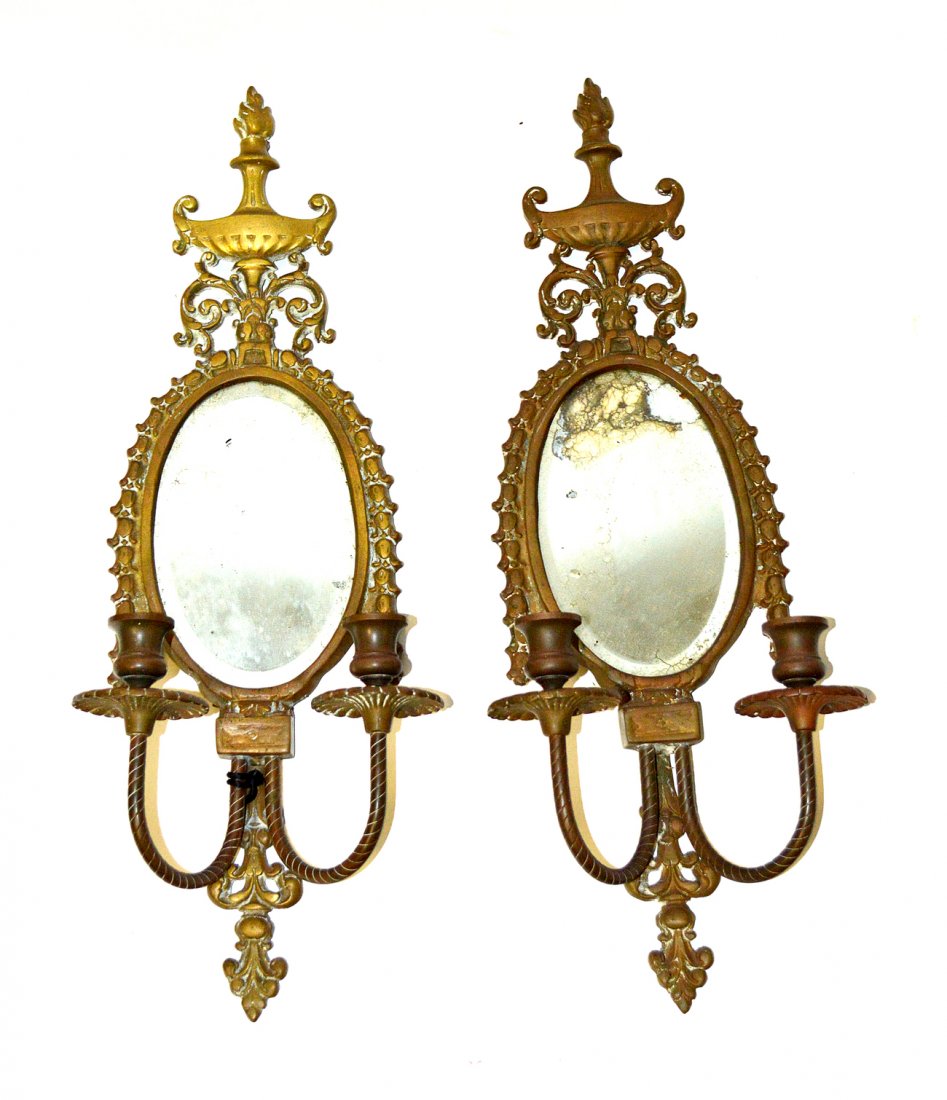 Pair of Mirrored Sconces: Pair of bronze sconces with oval back, garland decor and torch form finials. 23 1/3"H x 9"L. One mirror very worn. Sconces need cleaning.