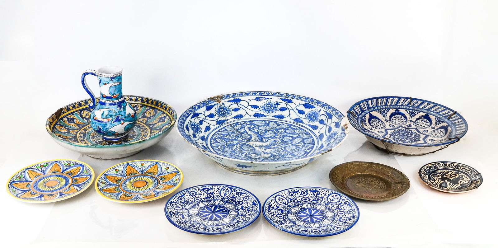 Large Group of Majolica Serveware: Group of serveware, including three large Spanish or Moroccan Mooresque majolica chargers, two sets of Spanish majolica plates, one decorative Mexican plate, one brass plate and one Turkish pottery ju