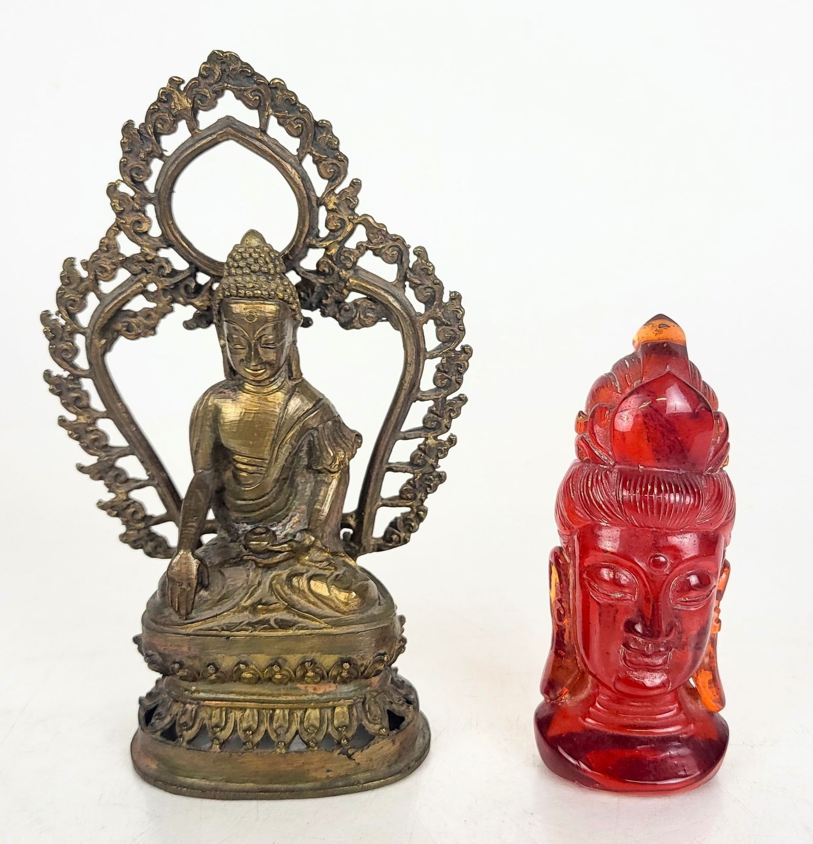 Two Buddhist Objects: Two small Buddhist decorative objects, including a molded resin imitation amber head from China and a Tibetan bronze statue of Buddha with flaming aureole. [Bronze: 7" H x 4 1/4" W x 3" D]. In good co