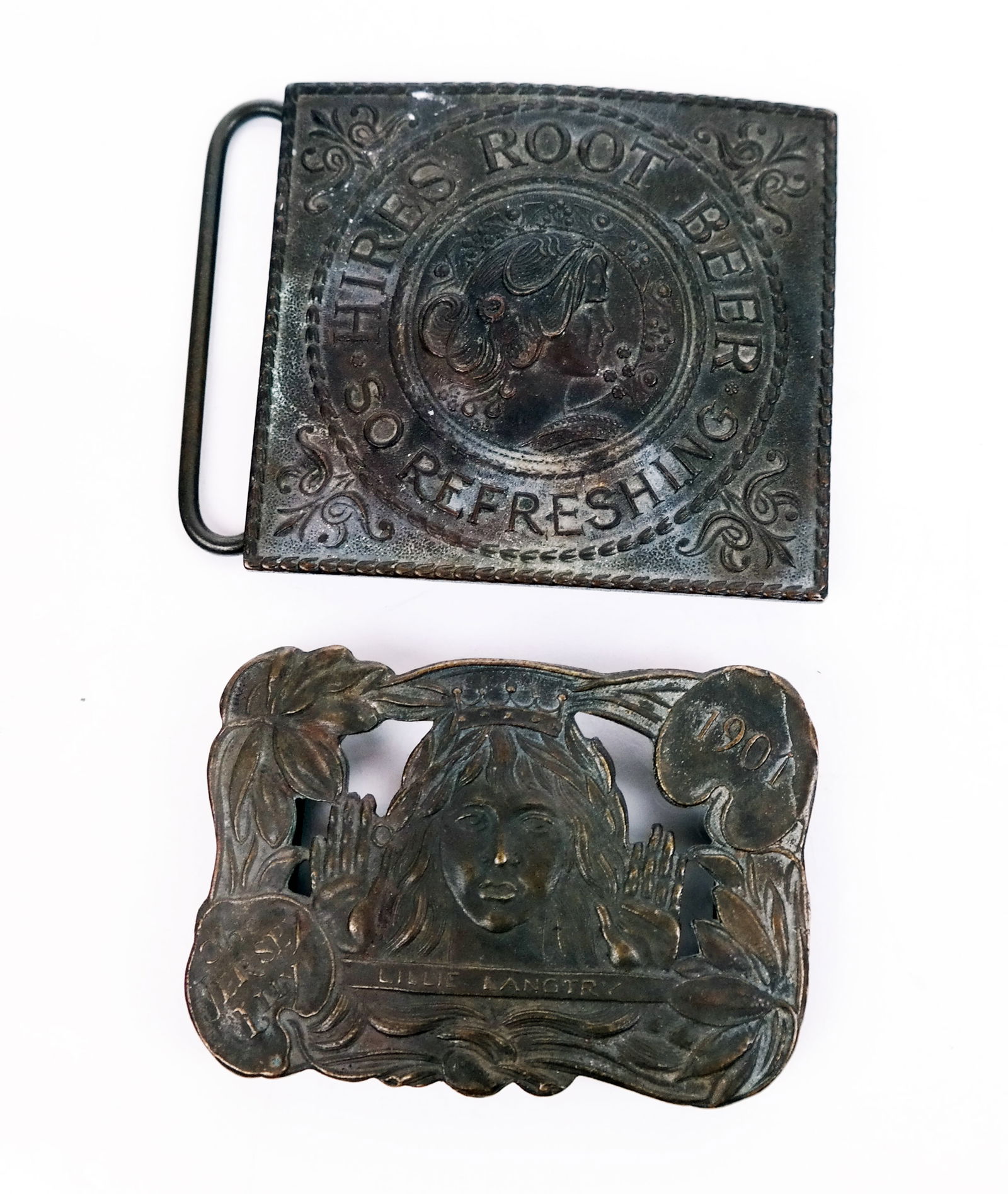 Two Tiffany Studios Metal Belt Buckles: Two (2) Tiffany Studios metal belt buckles, comprising a "Hires Root Beer", marked to base [2 7/8" H x 3 1/8" W] and a "1901 The Jersey Lily, Lillie Langtry", marked to base [2 1/4" H x 3 1/8" W]. Con