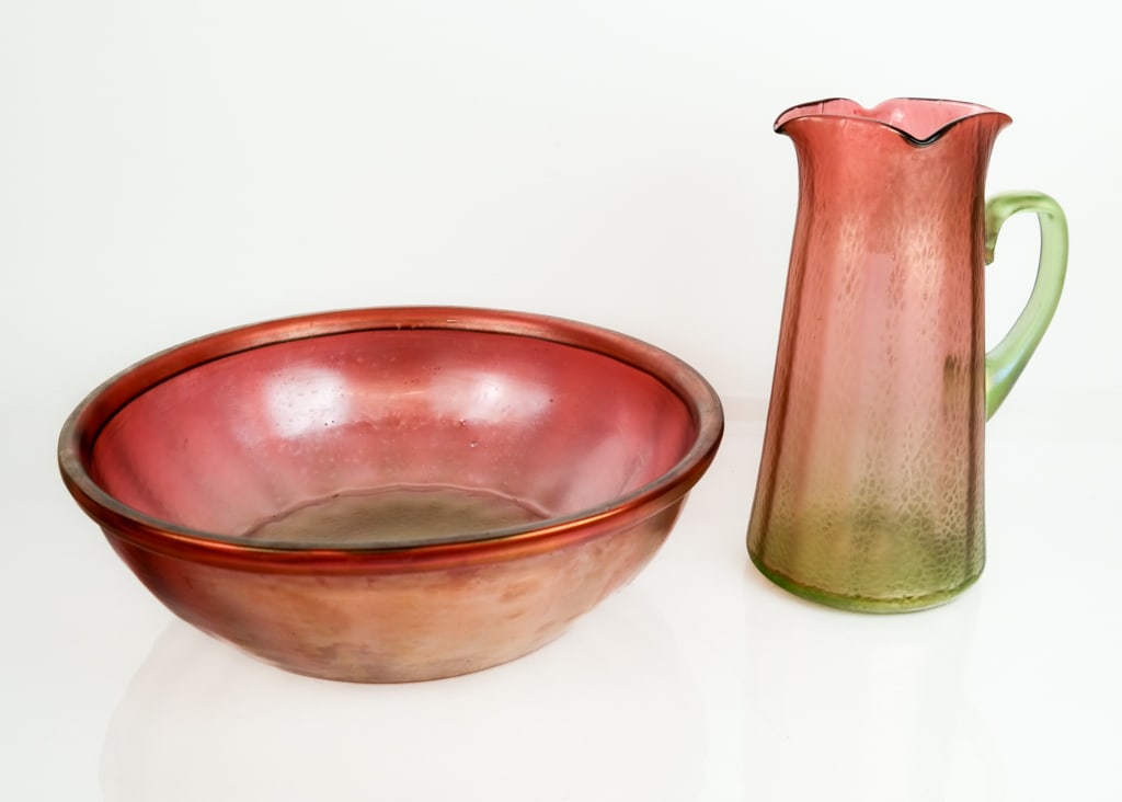 Loetz Manner Favrile Glass Washbowl and Pitcher: Loetz manner favrile glass Art Nouveau washbowl and pitcher, circa 1900, with a hammered finish. [Pitcher: 12" H x 8.5" W x 6.5" D]. Overall good condition with light wear to finish commensurate with