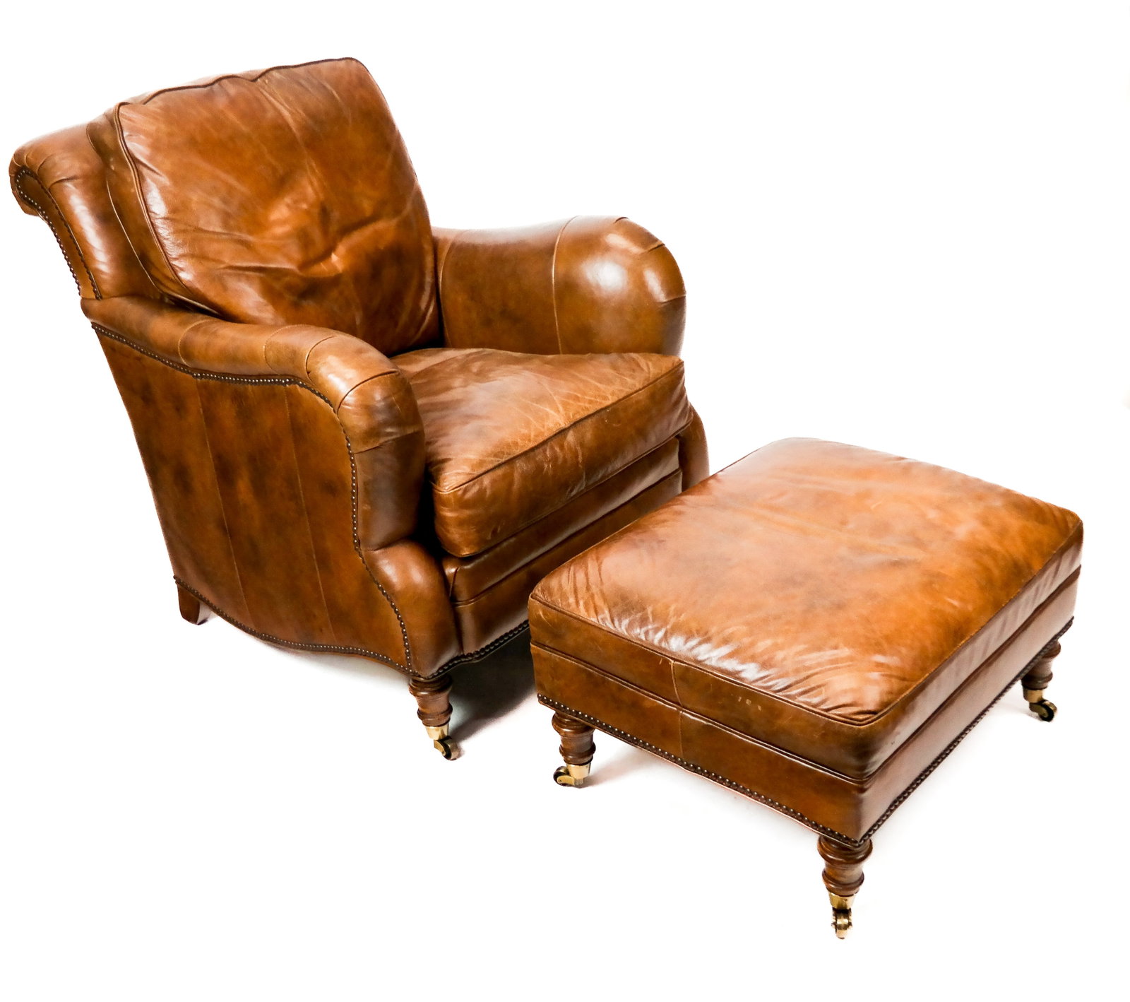 Stanford Furniture Leather Club and Ottoman: Stanford Furniture leather club and ottoman, in the English style and with castered feet; labels to bases [Chair 35.75" H x 31" W x 36", 20" to seat; ottoman: 14.5" H X 26" W X 22"] Worn/stressed cond