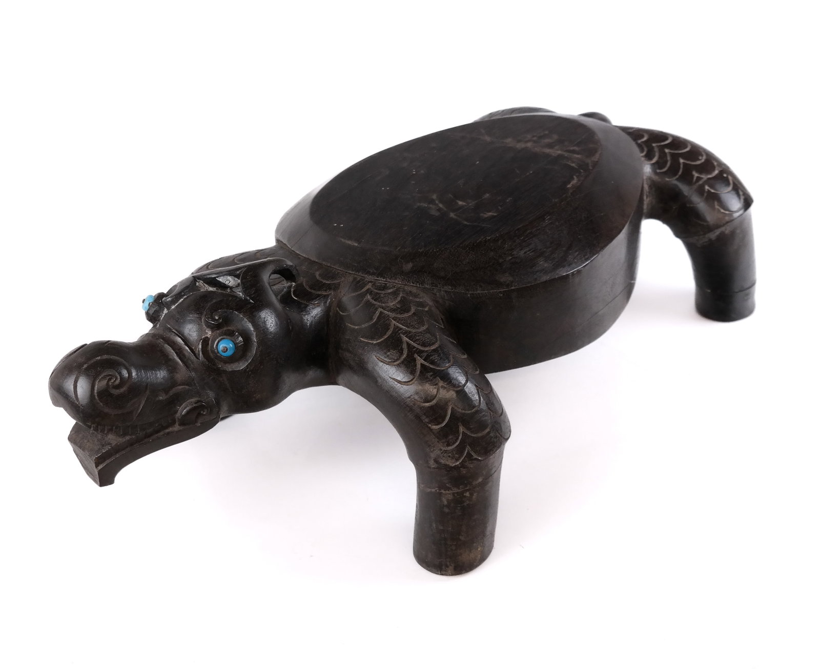 Indonesian Carved Tropical Wood Ottoman: Indonesian carved tropical wood ottoman in the shape of a turtle with blue decorative eyes. [7.5" H x 12.5" W x 23.5" L]. Overall good condition with some fading to finish and repairs to the front and
