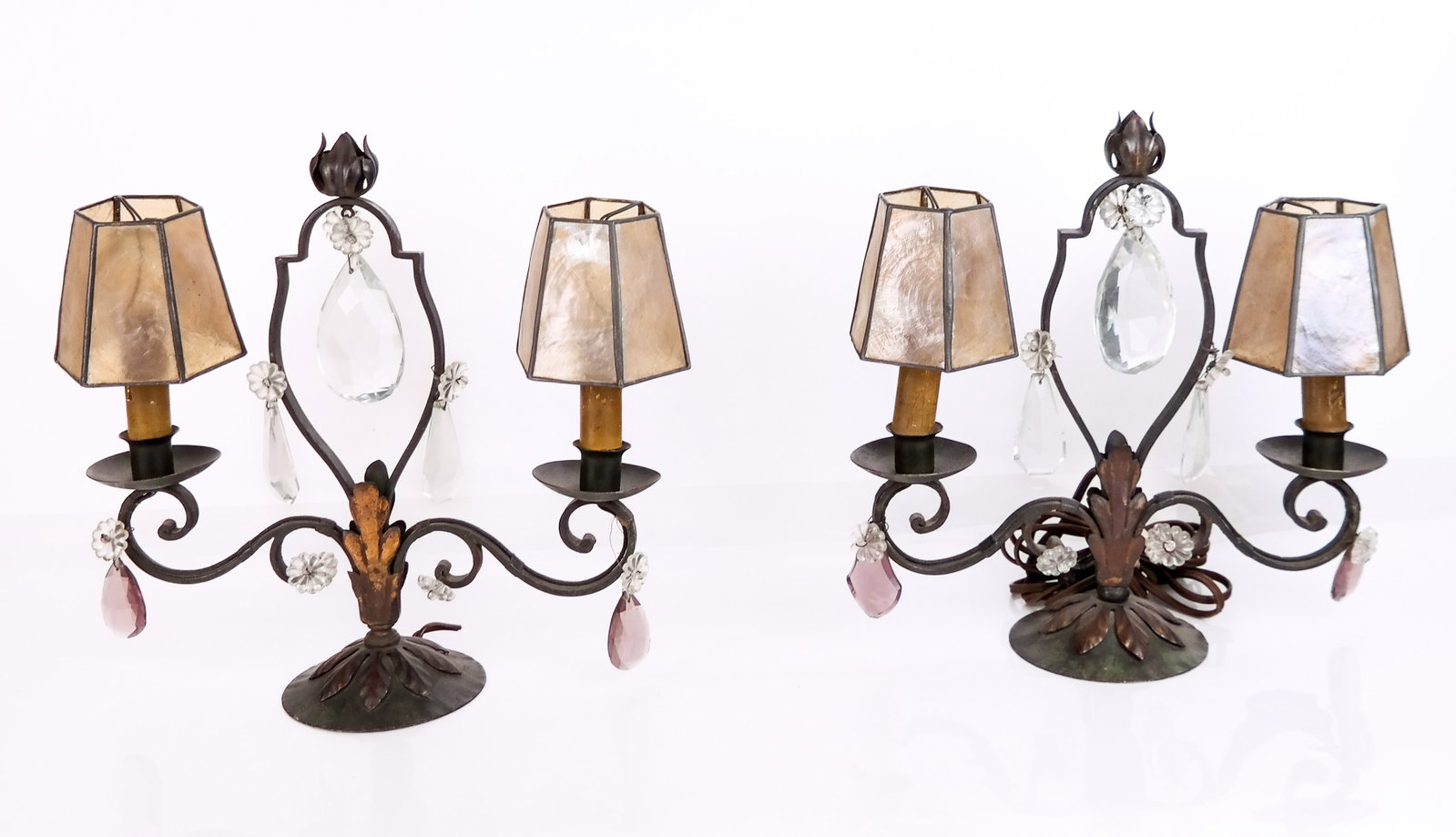 Pair of Wrought Iron Girandole Lamps: Pair of French-style girandole lamps with mica shades and crystal prisms in wrought iron frames. [13" H x 12" W x 5" D]. Condition reports and requests for additional photos cannot be accepted on this