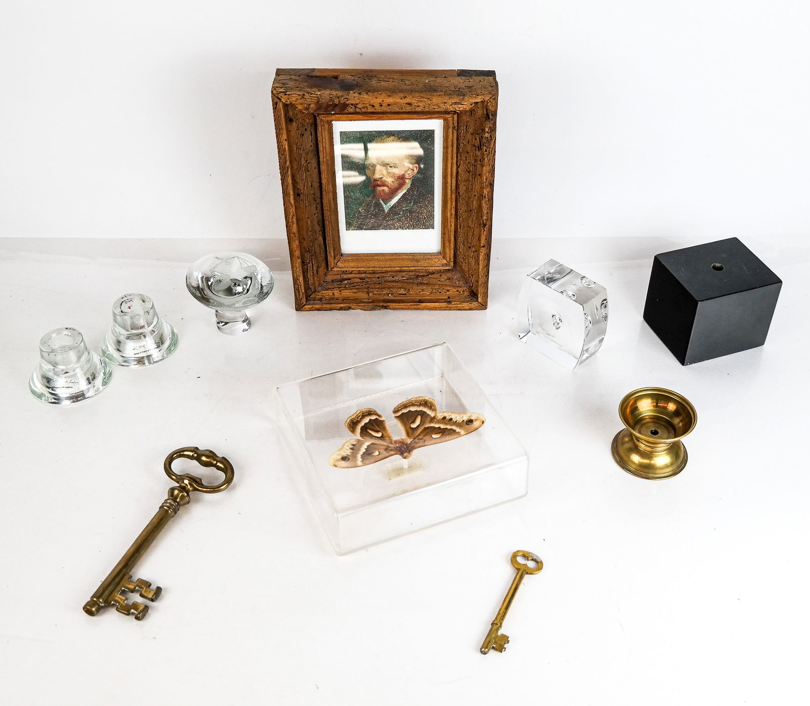 A Group of Decorative Objects, 9: A group of decorative objects including a moth in a frame, two glass candle holders, a glass mushroom marked "Libra", two oversize brass keys, a small black stand, a small brass stand, an art glass pa