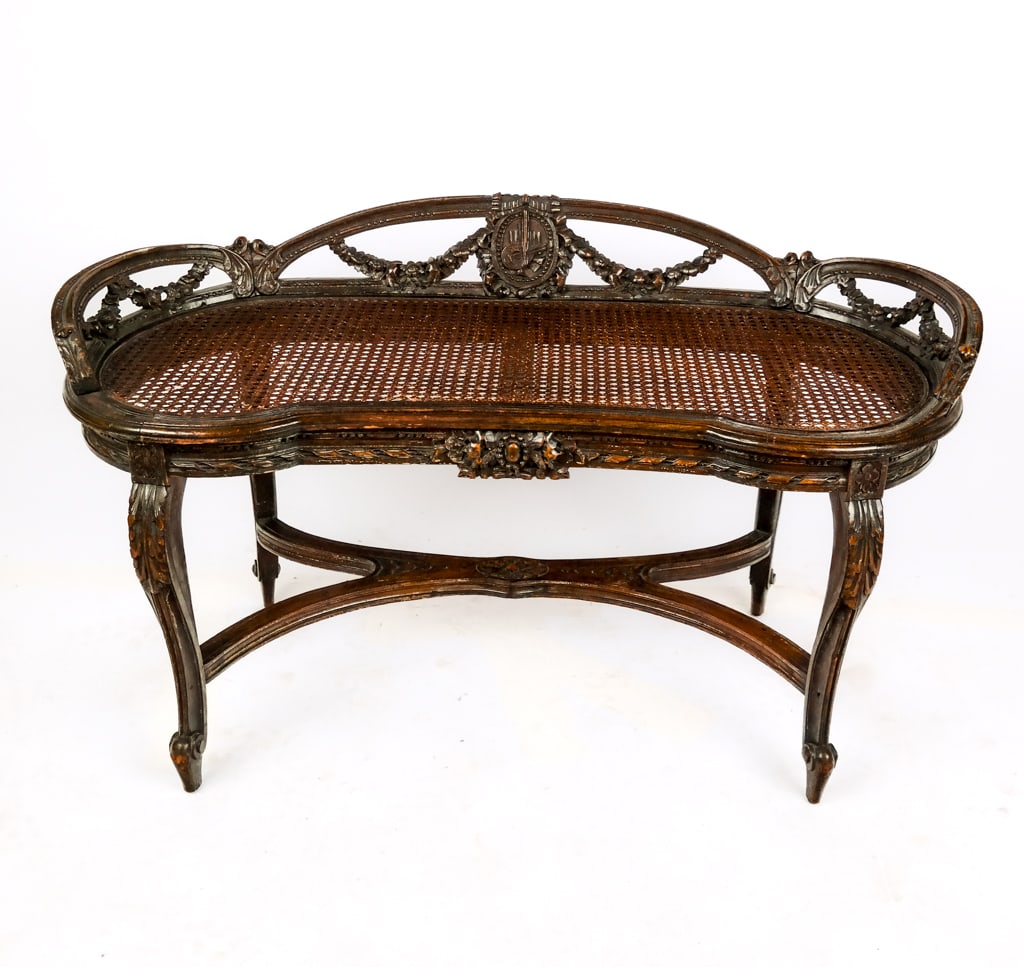 Louis XV Carved and Caned Loveseat: Louis XV carved, painted and caned loveseat or window seat, 20th century, with foliate decorations throughout, crossing braces at legs, and a mandolin medallion in center [24" H x 41.5" W x 18.5" D] O