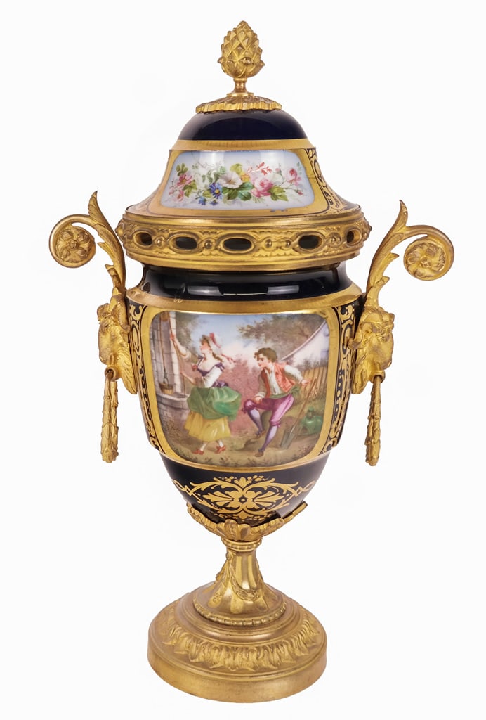 Cobalt Blue and Bronze Mounted Porcelain Urn: Cobalt blue and bronze mounted porcelain two-handled urn, circa 19th/20th century, with floral decorated cartouches, goat mask handles, and a artichoke finial; spurious marks to inner lid. [14" H x 8.
