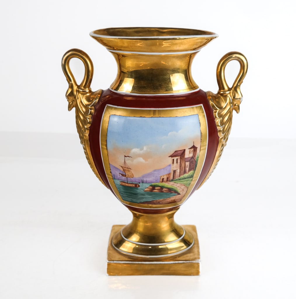 Porcelain Hand-Painted Vase with Seascape: Porcelain hand-painted vase with two handles and a seascape, French, with a gilt base, lid, and handles, having an oxblood background color with seascapes of boats near buildings on both sides and swa