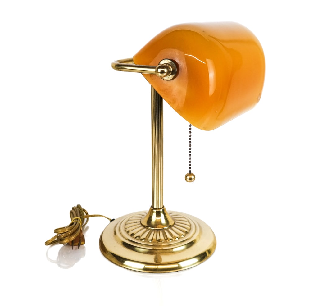Amber Glass Banker's Lamp: Amber glass banker's lamp, mid-20th century, with an amber glass shade over a brass base with a chain pull and Underwriters Laboratories sticker affixed to base. [14" H x 11" W x 10" D]. Overall condi