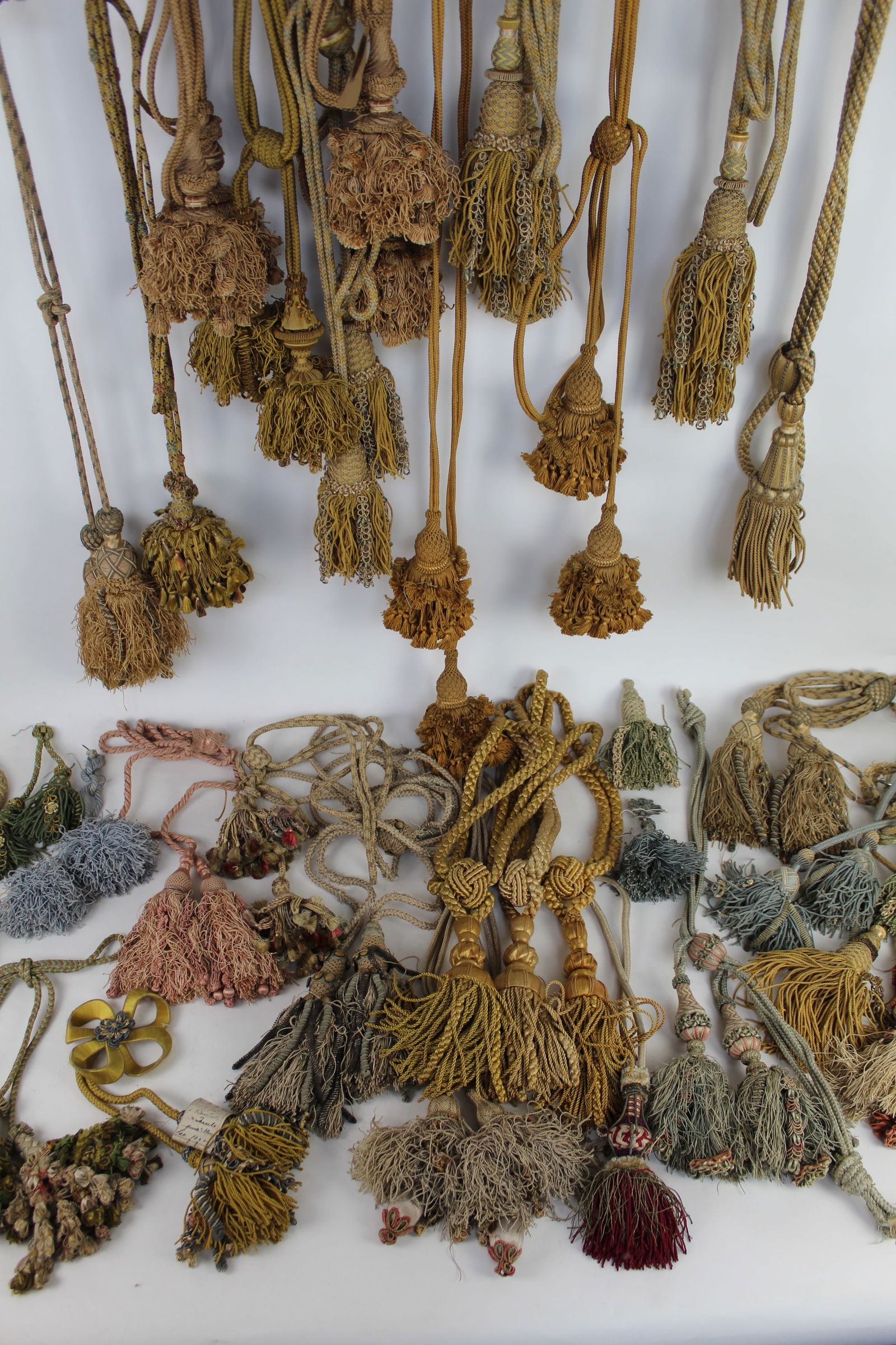 Collection of Antique Upholstery Silk Tassels: Large collection of antique silk tassels, most paired, including two groups of large and small looped silk fringe tassels on braided cords, in golden ochre and pale tan; three large yellow silk tassel