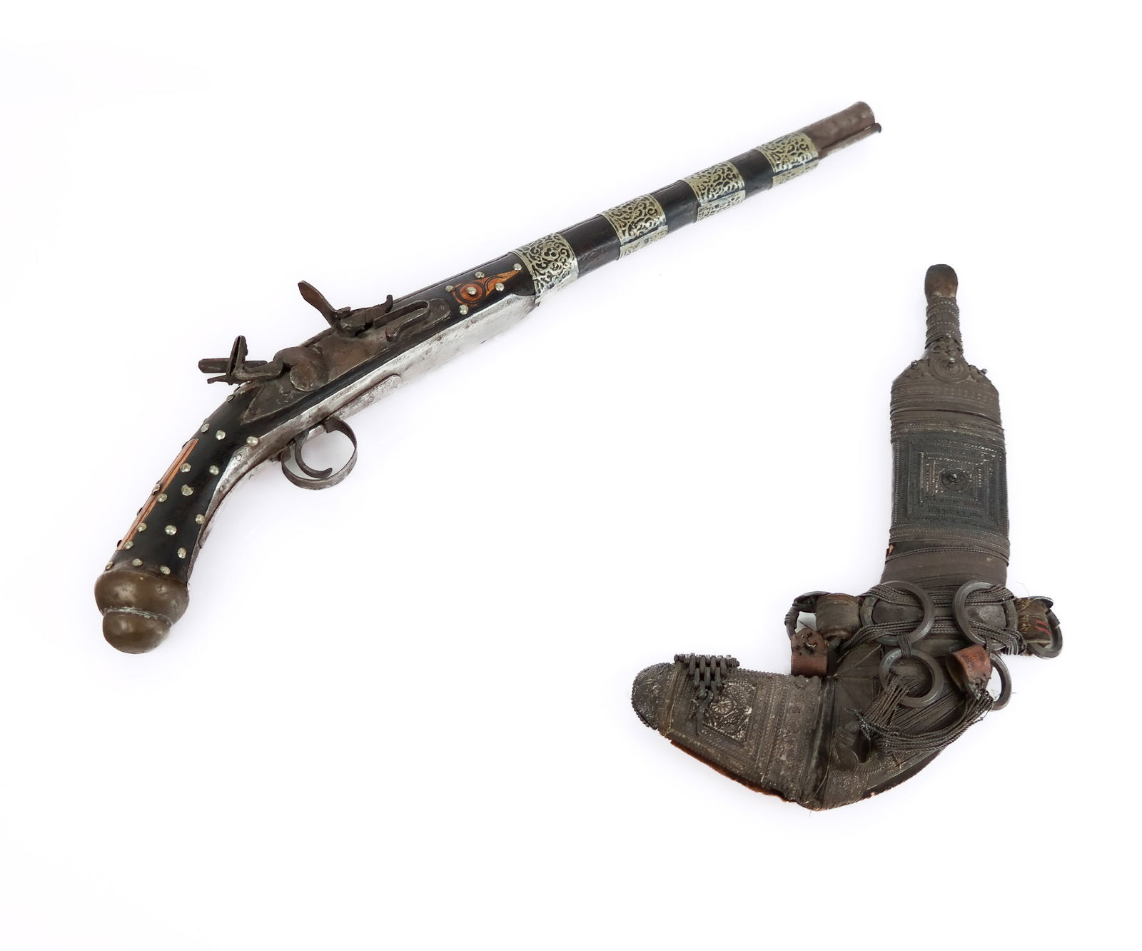 Two Middle Eastern Weapons: Two Middle Eastern decorative weapons comprising an Omani Jambiya knife, and a bone inlaid flintlock pistol, likely Moroccan. [Pistol: 21" L x 6" H x 1.5" D]. Overall condition as is with wear and ant