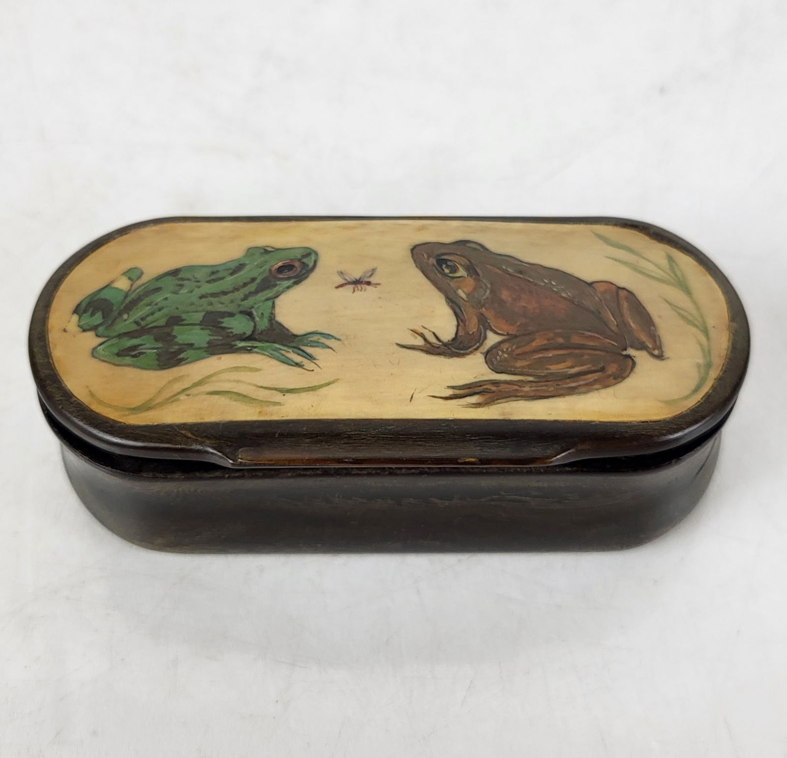 Inlaid Box with Frog Decoration: Inlaid wood box with hand-painted frog decoration to lid, 20th century, with bone inlay. [1" H x 3.75" W x 1.75" D]. Overall condition is fair with cracking to wood, warp at hinge, and a loss to paint