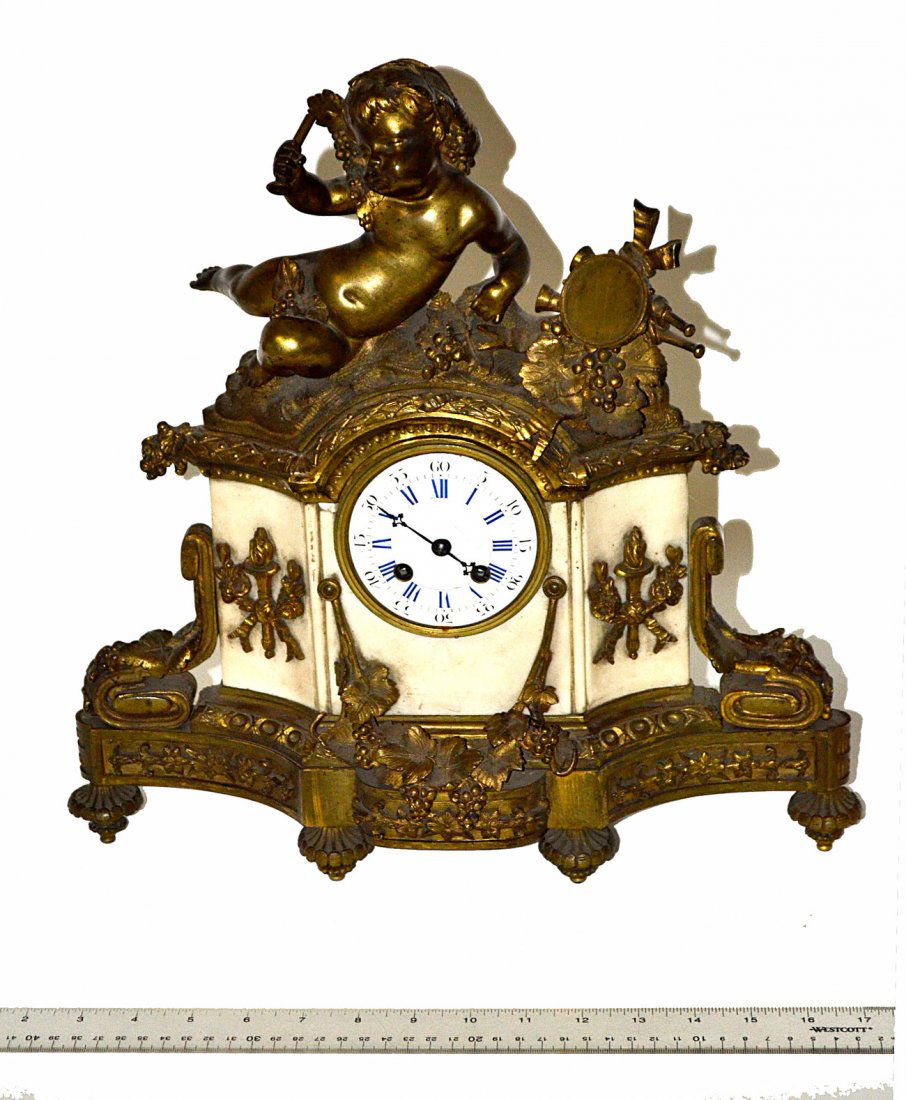 Bronze and Alabaster Mantle Clock: Vintage enamel face plate mantle clock with Neoclassical bronze mounts featuring an elaborate Bachanalian Putto pediment. As is. [15 3/4" W x 5 1/2" D x 15 3/4" H]