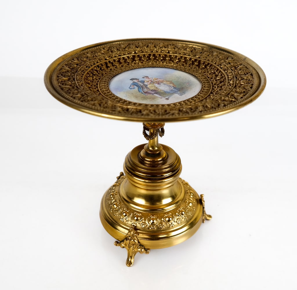 Gold-Tone and Enamel Three-Footed Tazza: Gold-tone metal and enamel three-footed taza, featuring imagery of a man and woman in 18th century attire in a field on enamel surrounded by gilt pierced foliate and avian imagery on the top of the ta