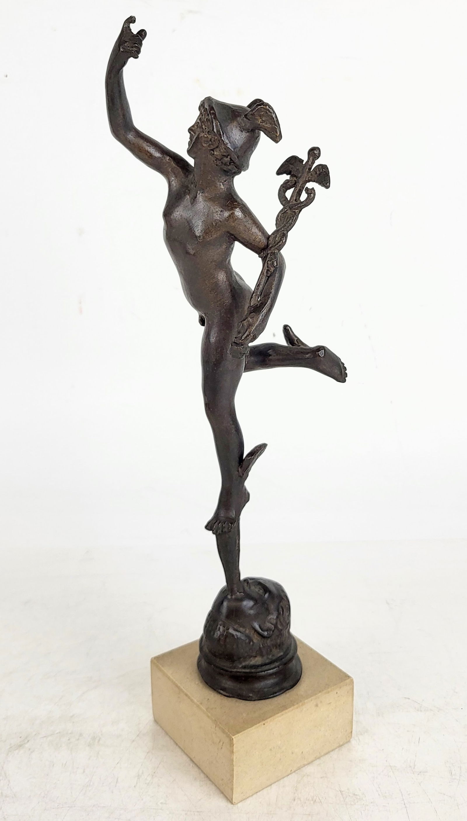 After Giambologna Flying Mercury: After Giambologna patinate metal figure of flying Mercury, 20th century, depicting a helmeted Mercury holding a caduceus, and floating atop Zephyr's breath, and supported by a travertine base. [13.75"