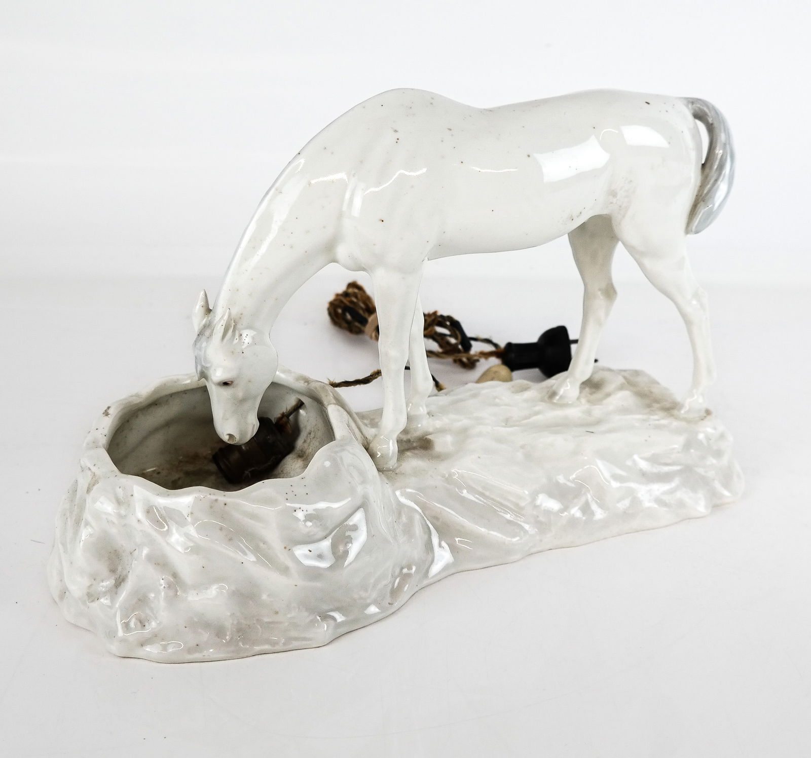 Porcelain Lamp in the form of a Horse: Porcelain lamp in the form of a horse at a pool of water, early to mid 20th century, marked illegibly to bottom. [8.5" H x 12" W x 8" D]. Condition is good with light wear; glass deficient. Estate of